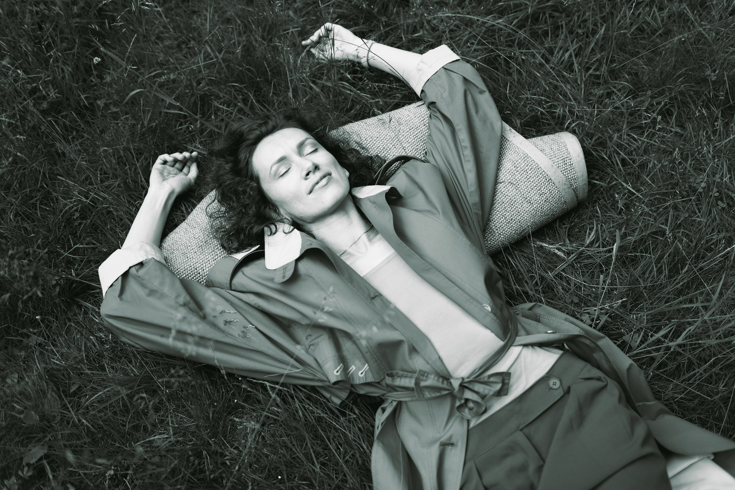 девушка в плаще лежит в траве, раскинув руки.