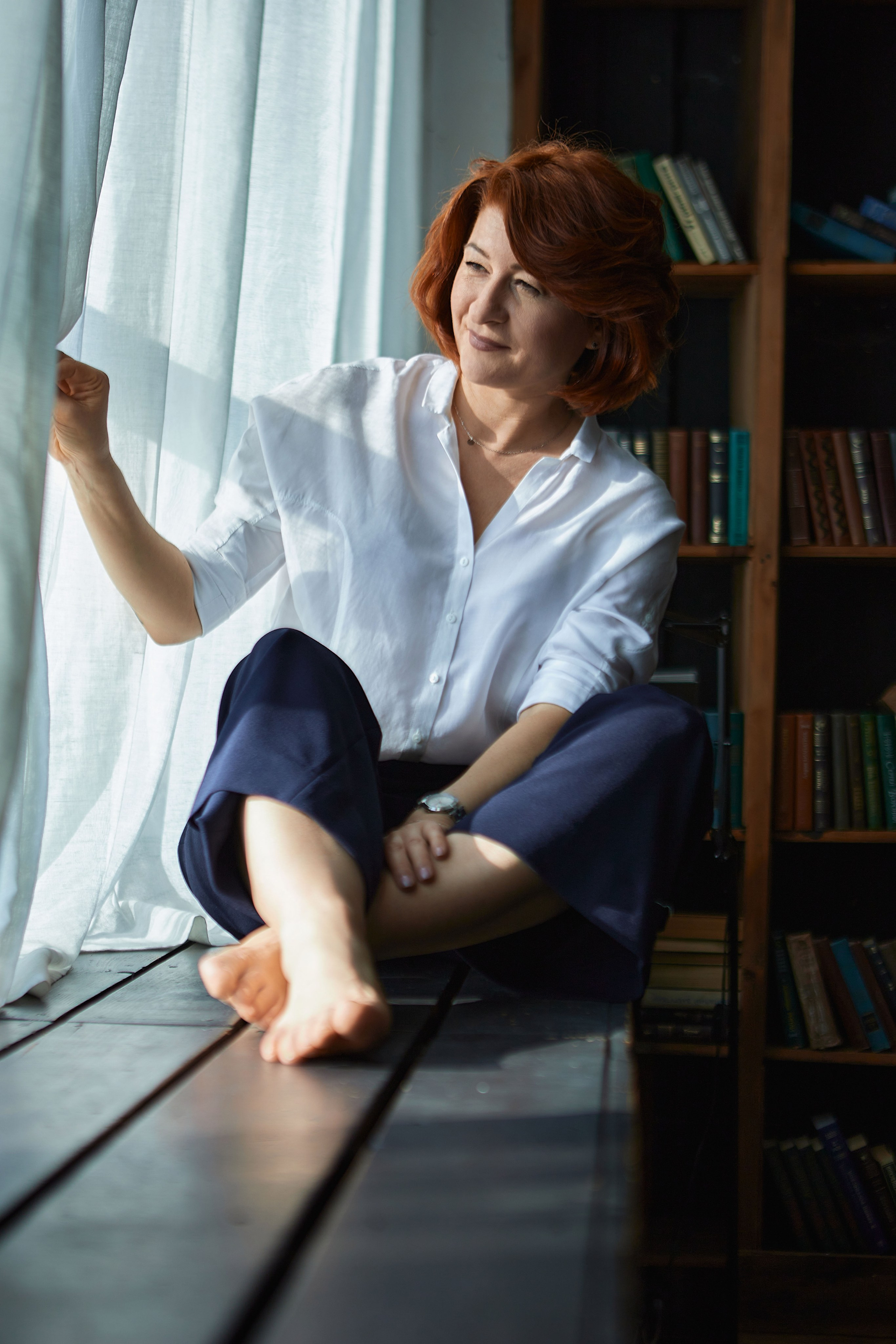 Женщина сидит на широком подоконнике и смотрит в окно