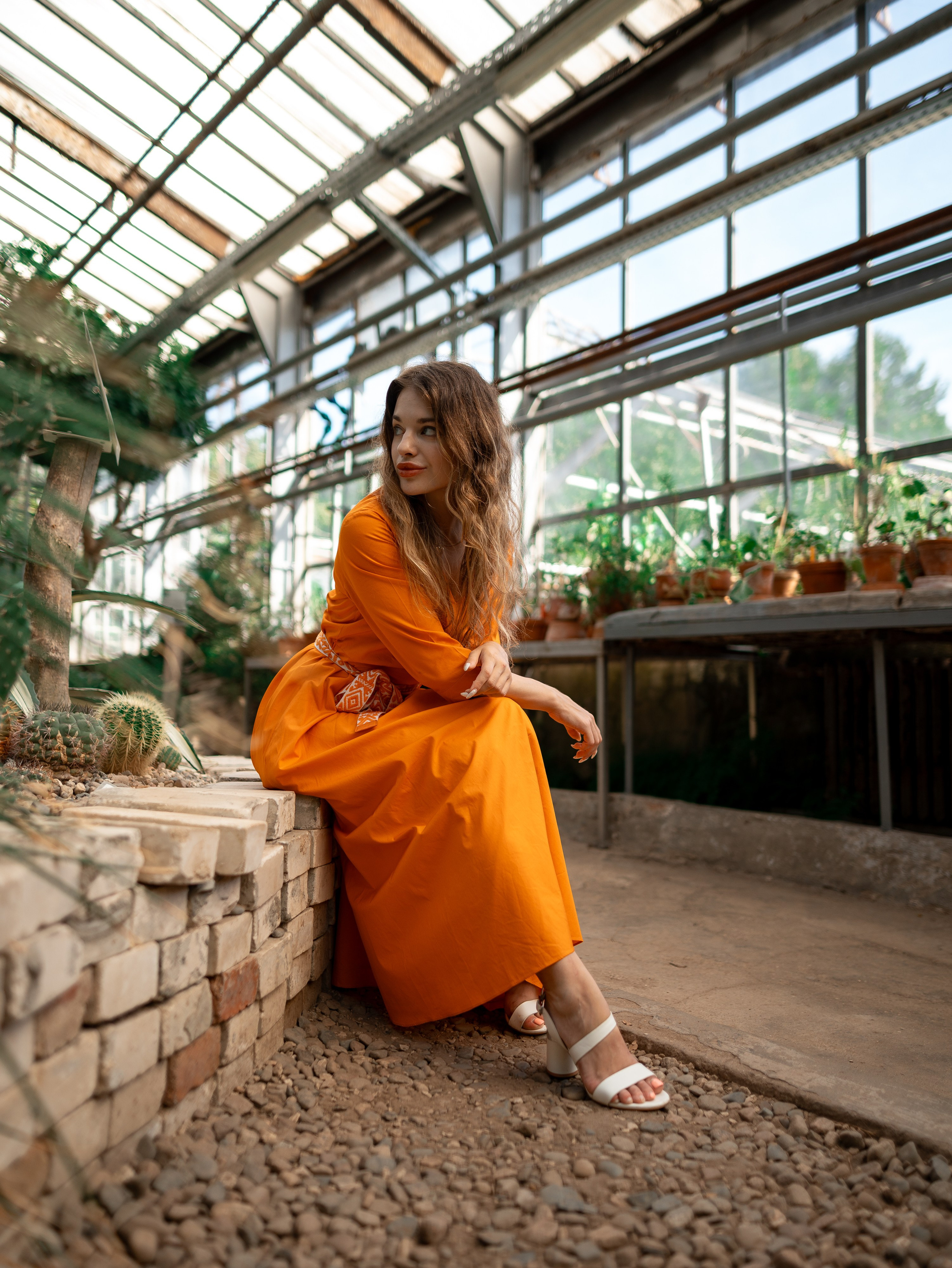 Девушка в оранжевом платье стоит на фоне зелени