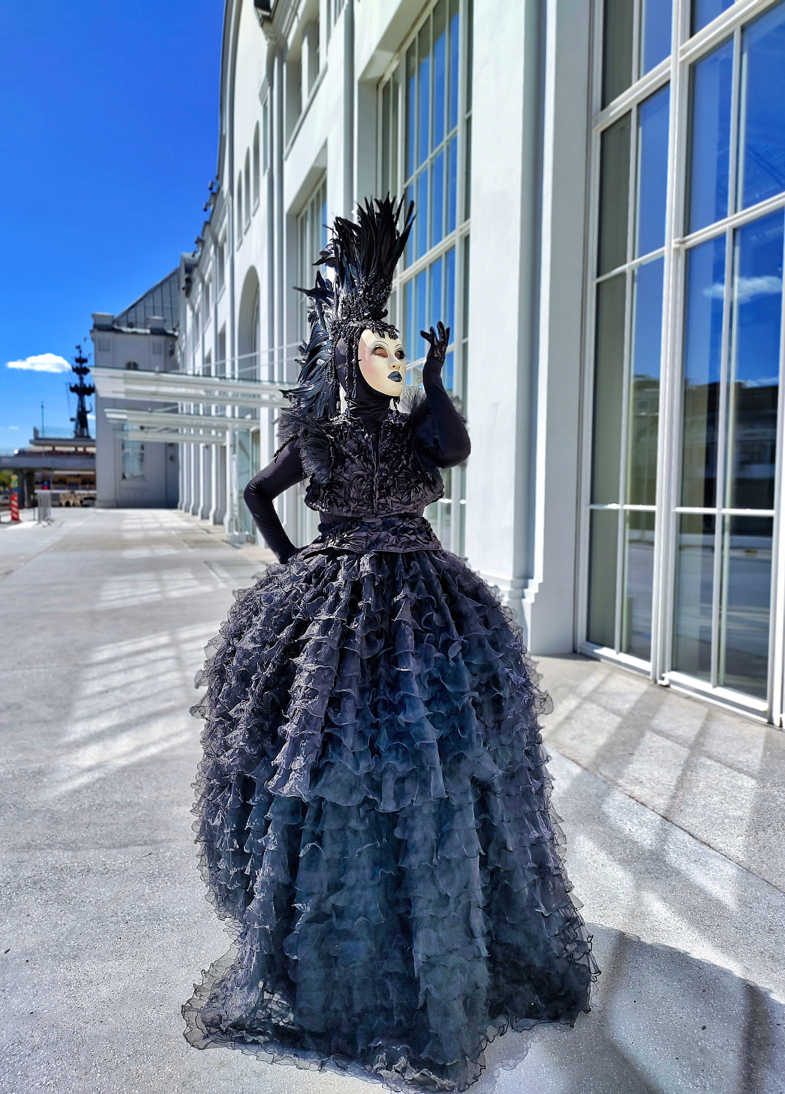 Организатор мероприятий смотрит из окна на артистку в широком платье и шикарной шляпе. 