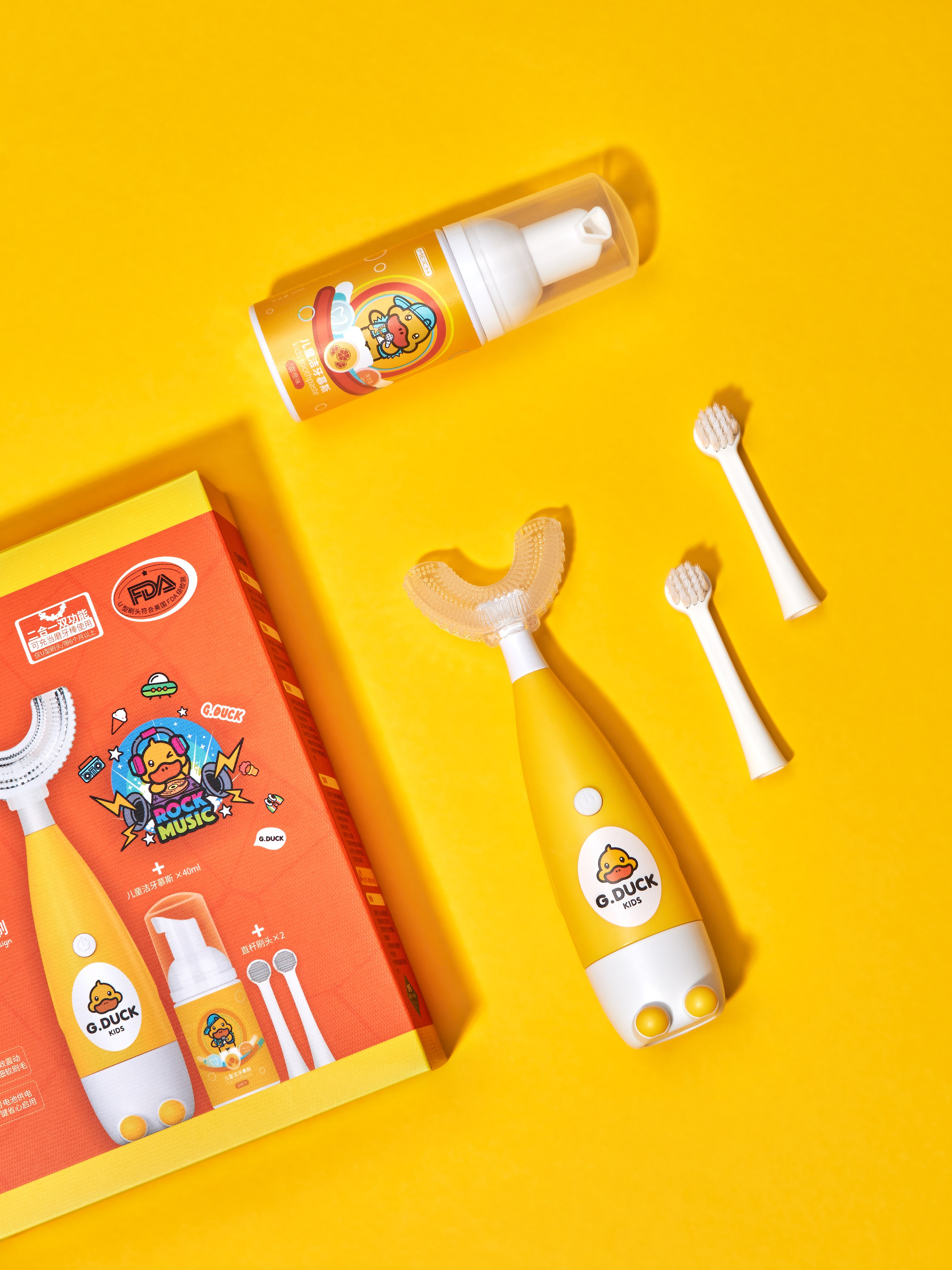Предметная фотосъёмка набора по уходу за детскими зубами с электрической детской зубной щеткой, пенкой для зубов, насадками для щетки, подарочной коробкой на желтом фоне