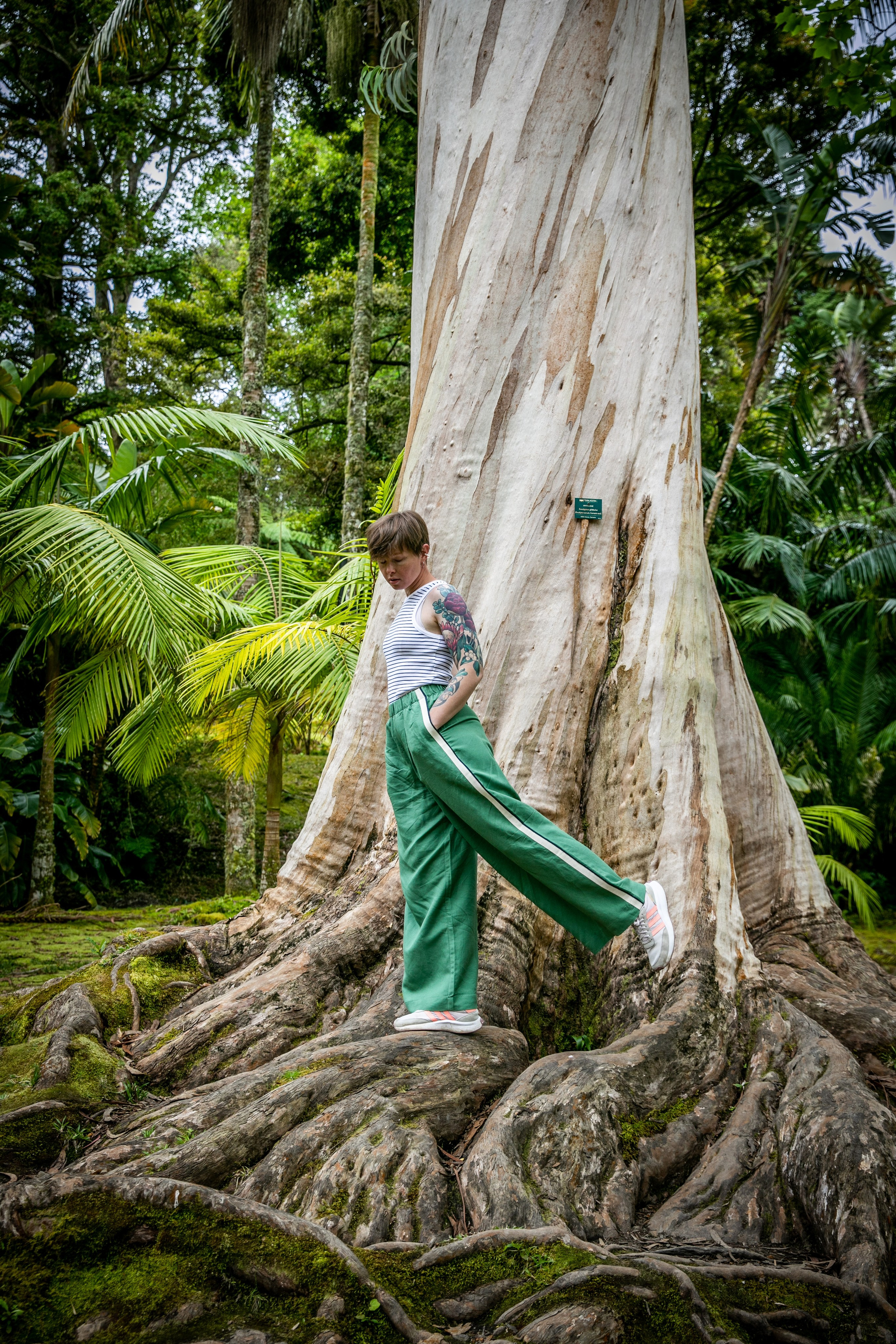 A young woman dressed in green trousers, exploring the stunning natural beauty of the Azores, with hills and the ocean around her