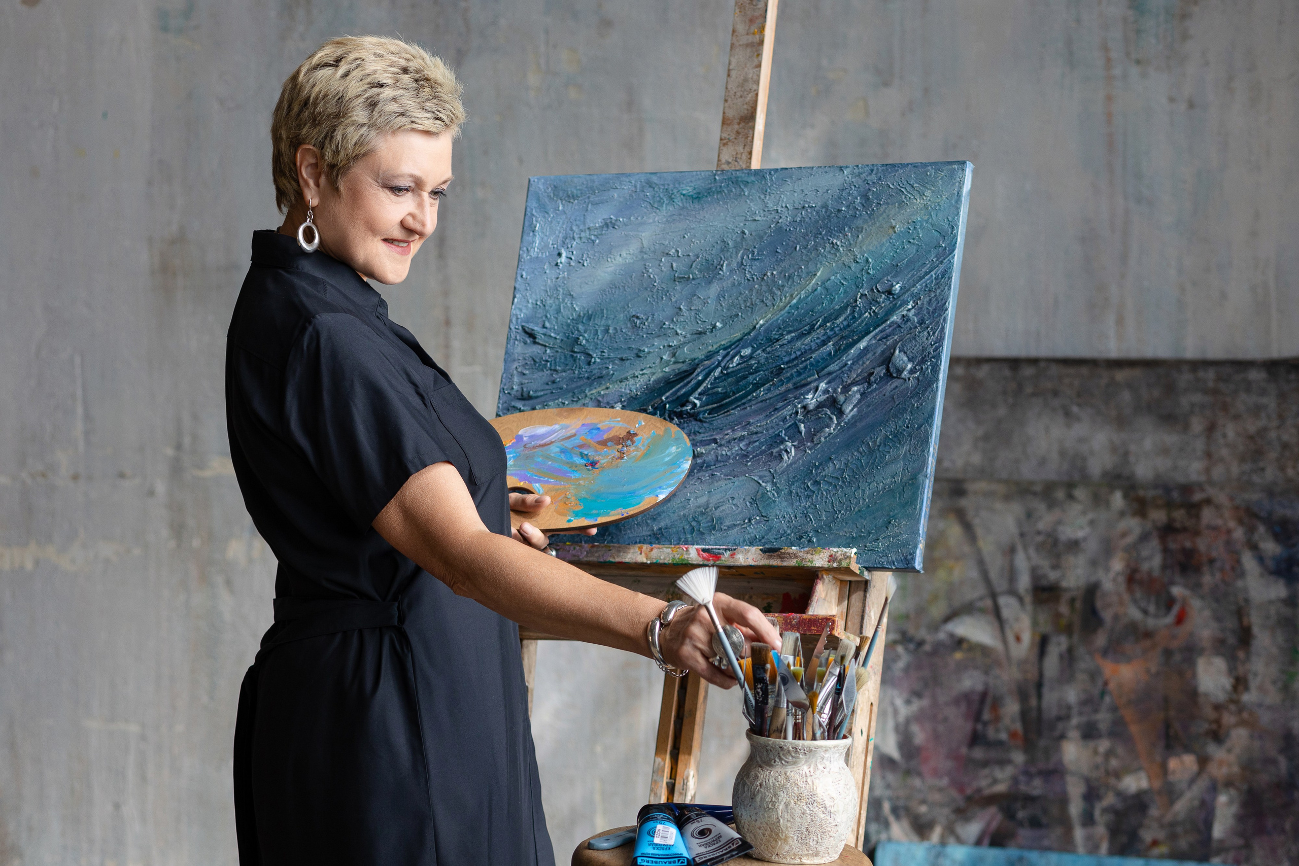 Женщина с палитрой стоит у пюпитра, выбирает кисть.