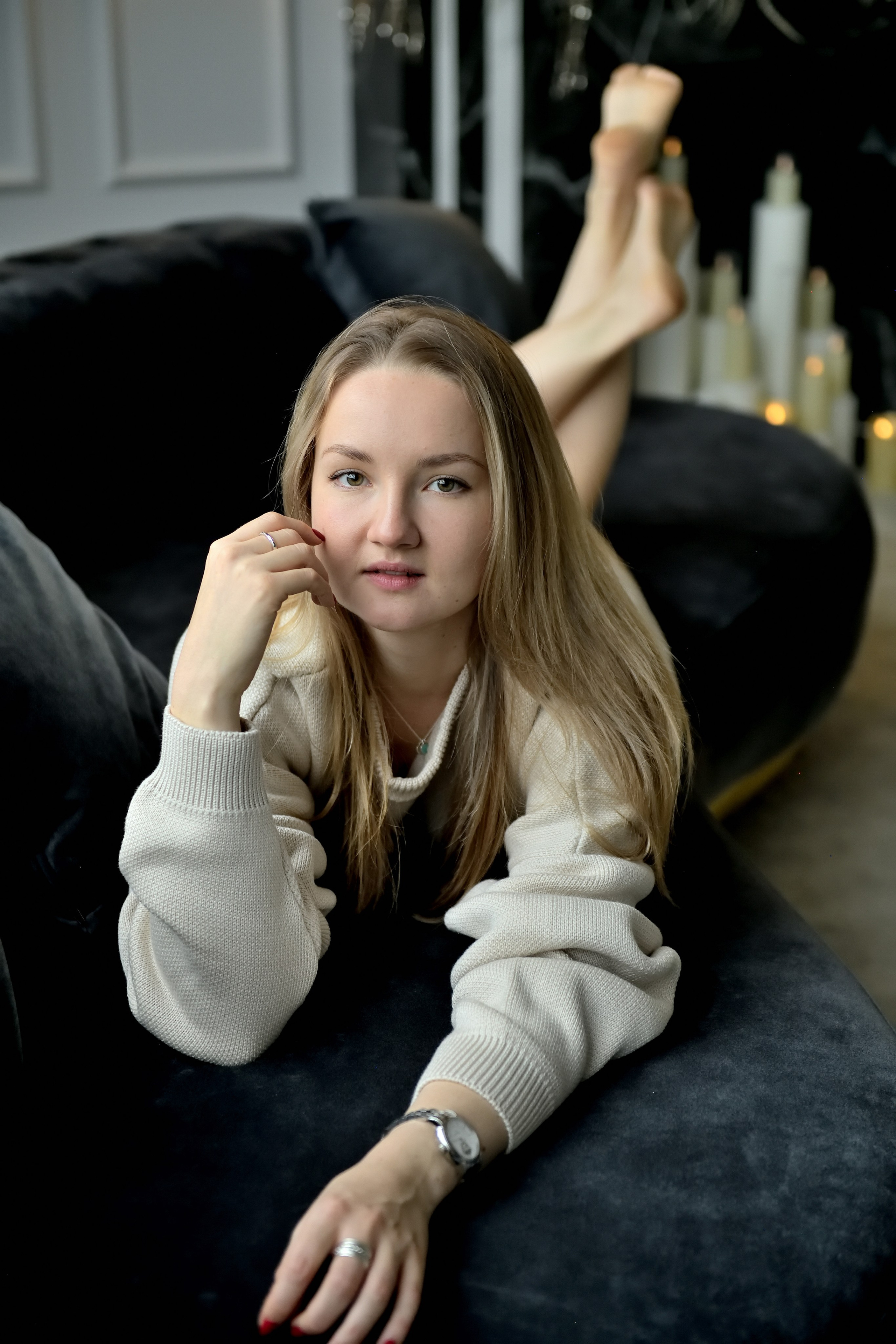 Девушка улыбается , смотрит в объектив и лежит на черном диване.