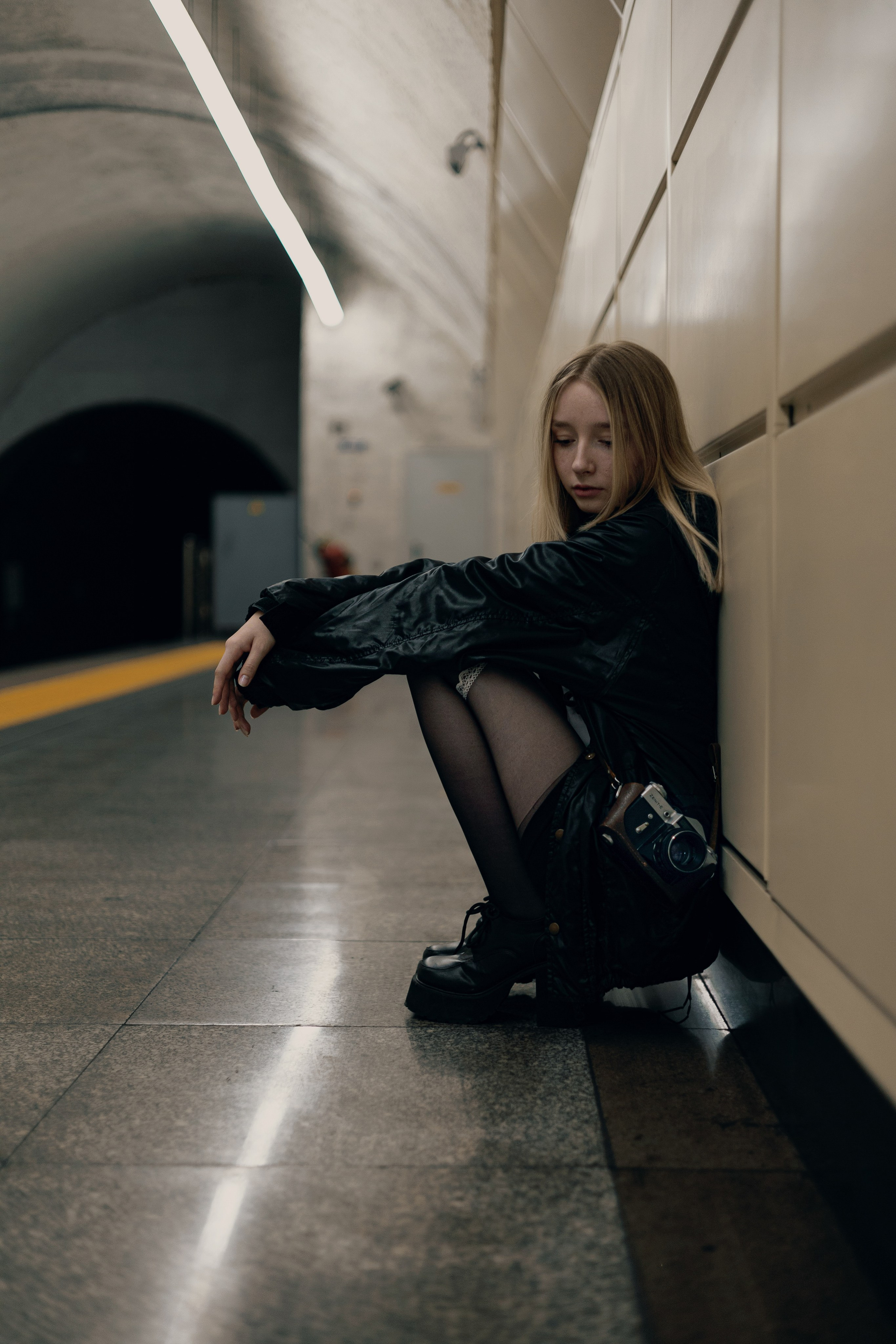 Фотосессия в метро — девушка в чёрной куртке сидит у стены станции