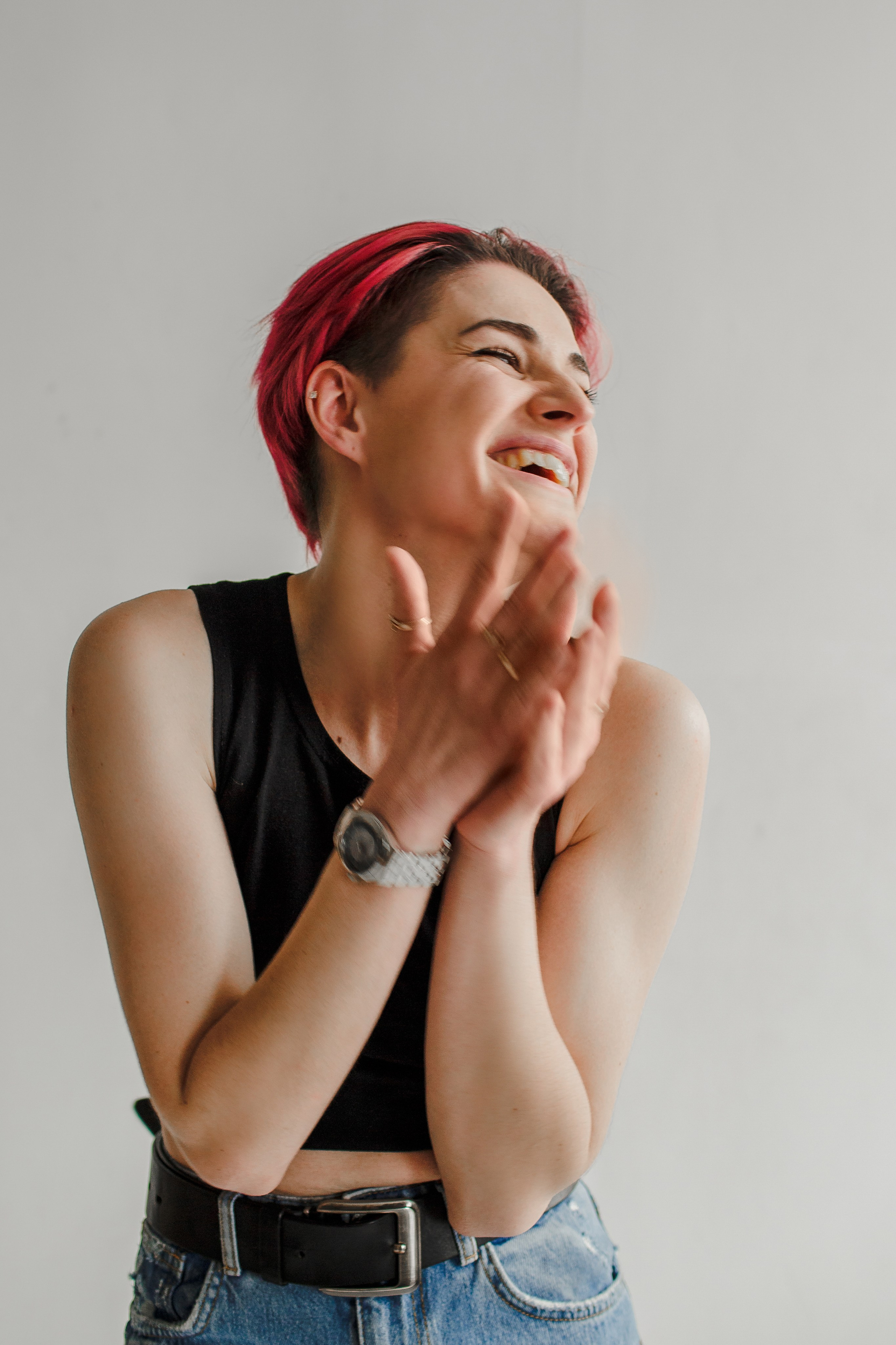 Молодая женщина смеется в зале с белыми стенами, свела ладони вместе.