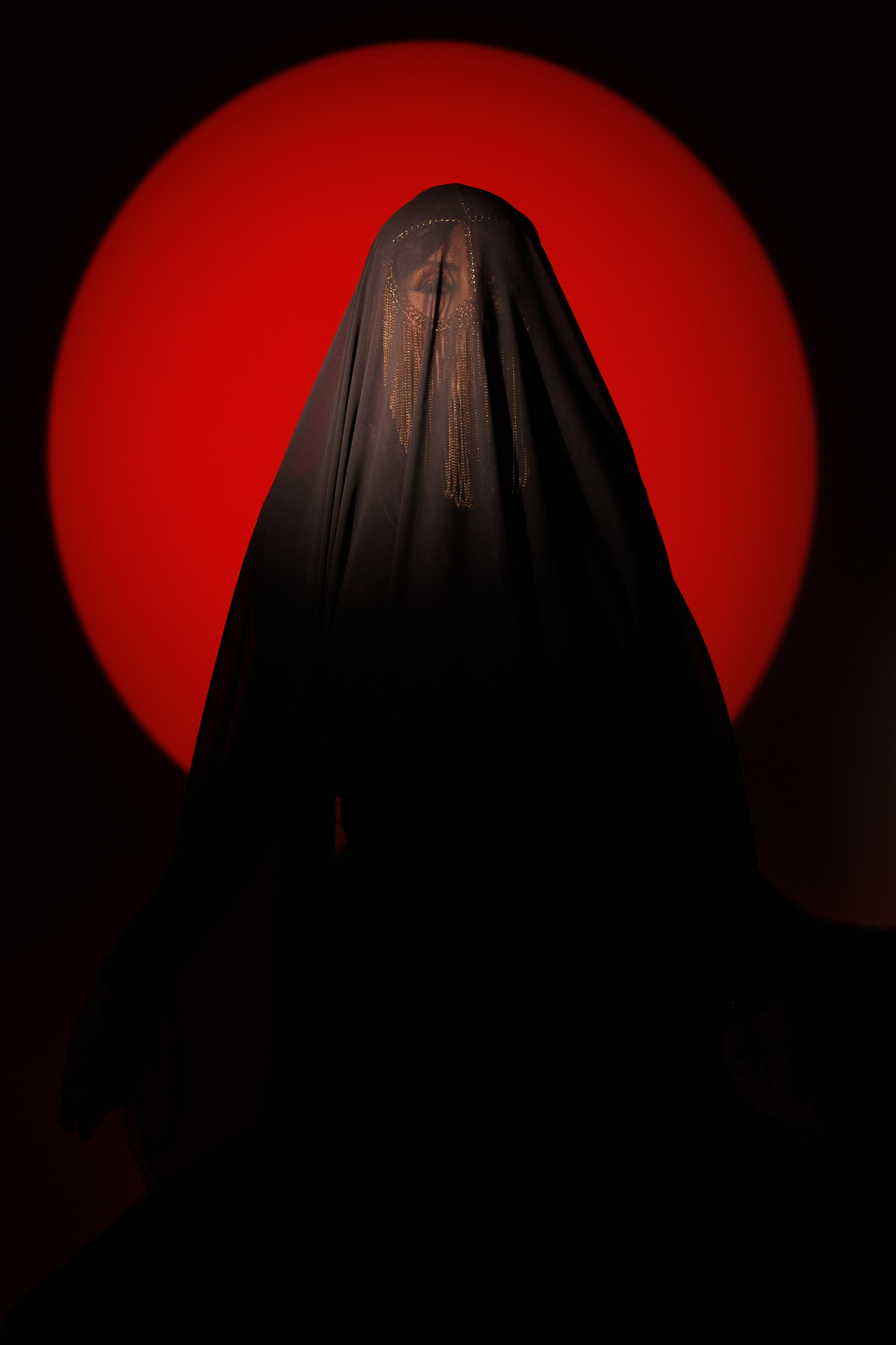 На фотографии изображена девушка в хиджабе, её лицо полностью закрыто, позади нее луч света напоминающий солнце