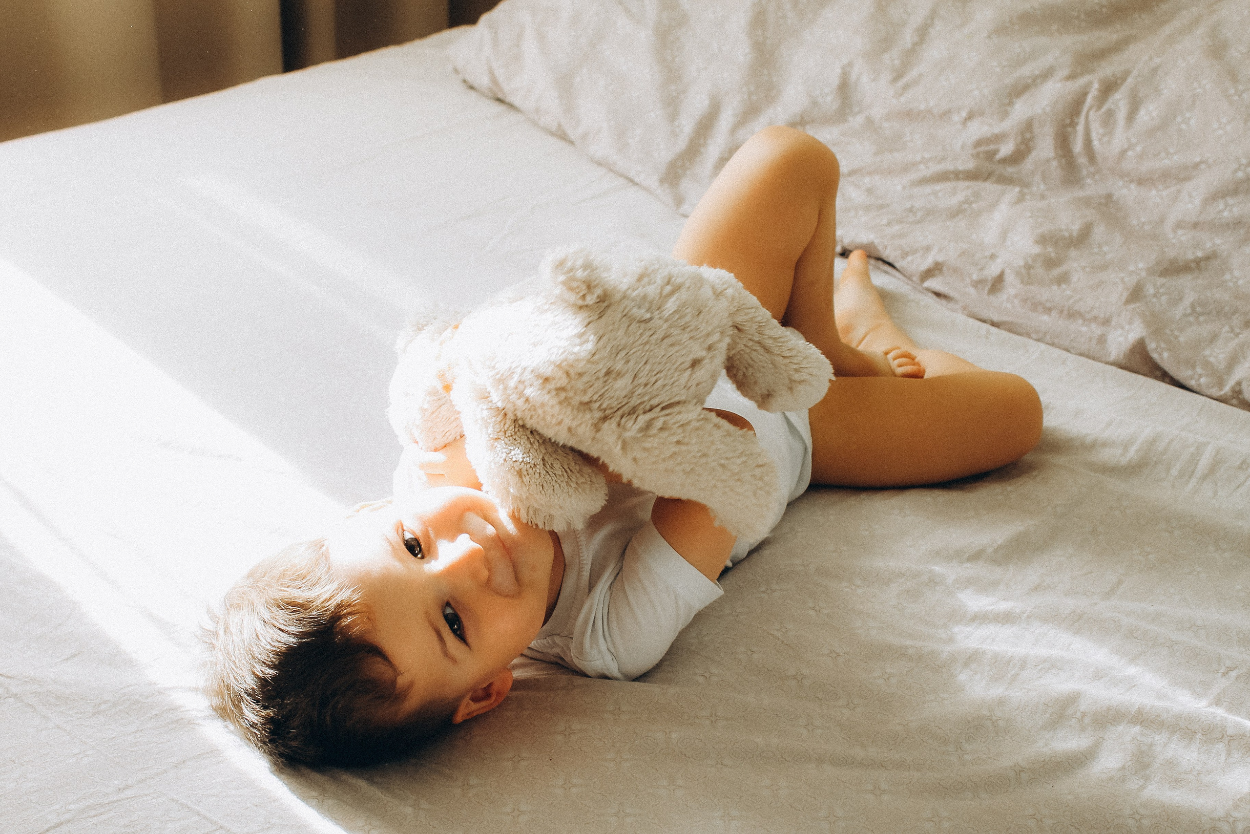 мальчик лежит на кровати с плюшевым мишкой