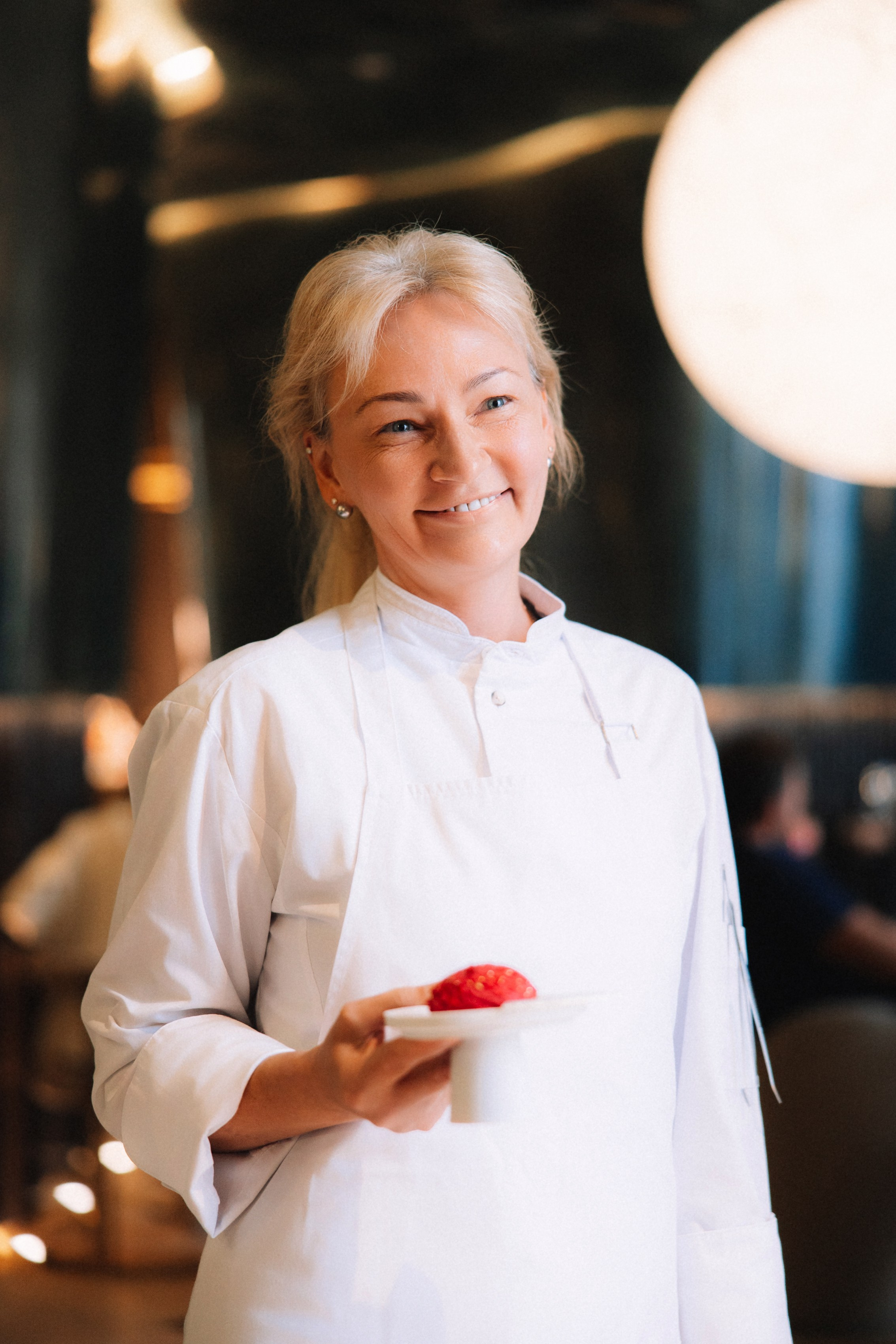 Команда: Девушка-повар в белом кителе с улыбкой представляет десерт.