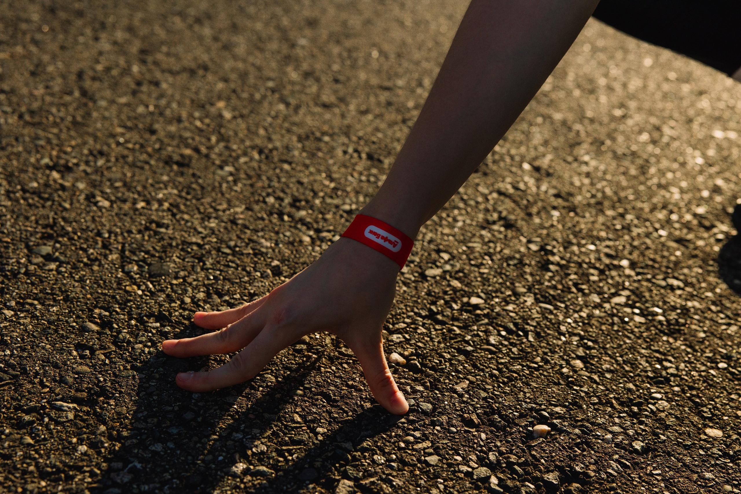 Акцент: Крупный план руки с красным браслетом участника на фоне текстуры асфальта.