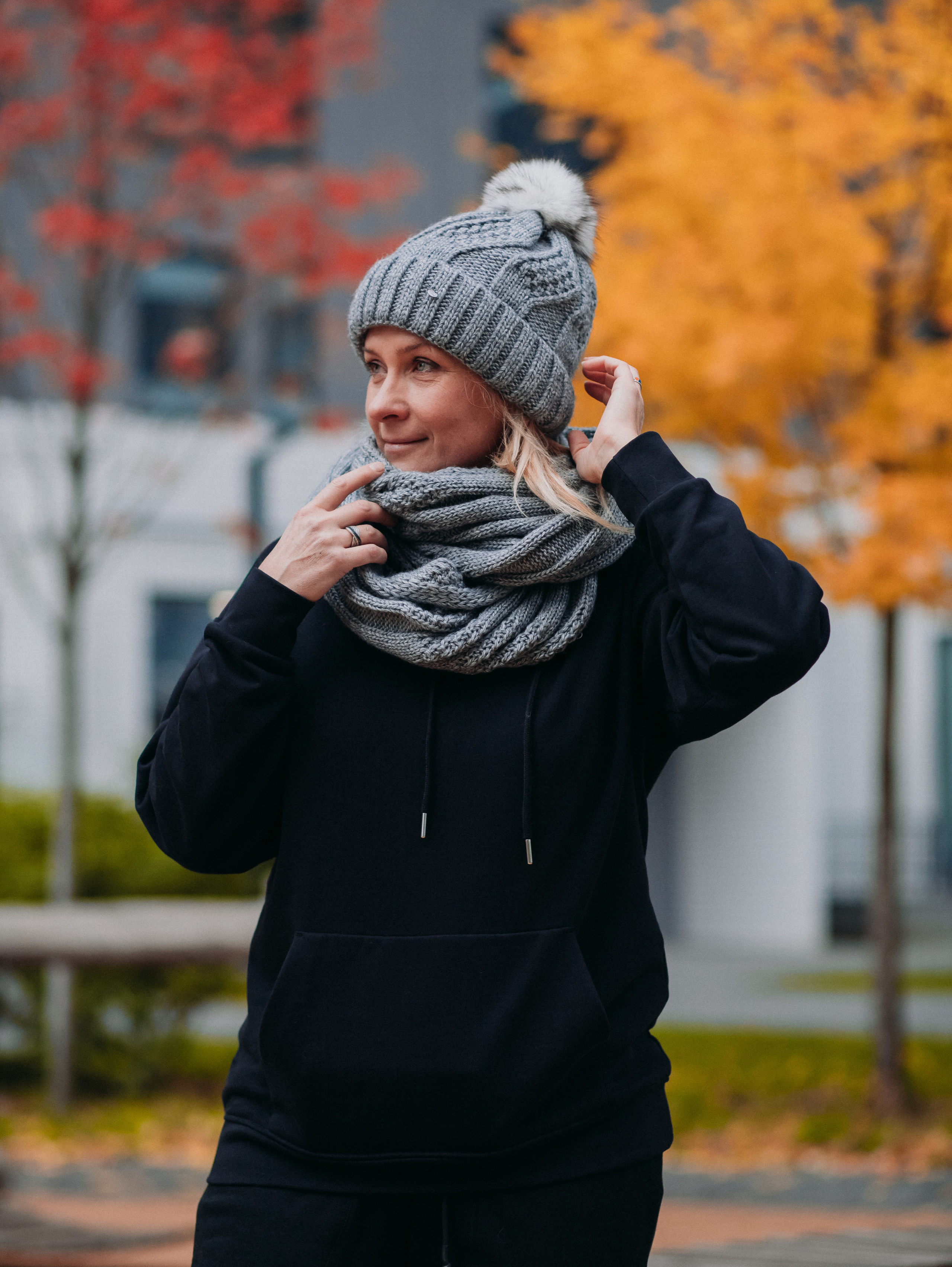 Девушка в шапке и в черном костюме на фоне на фоне осенних деревьев