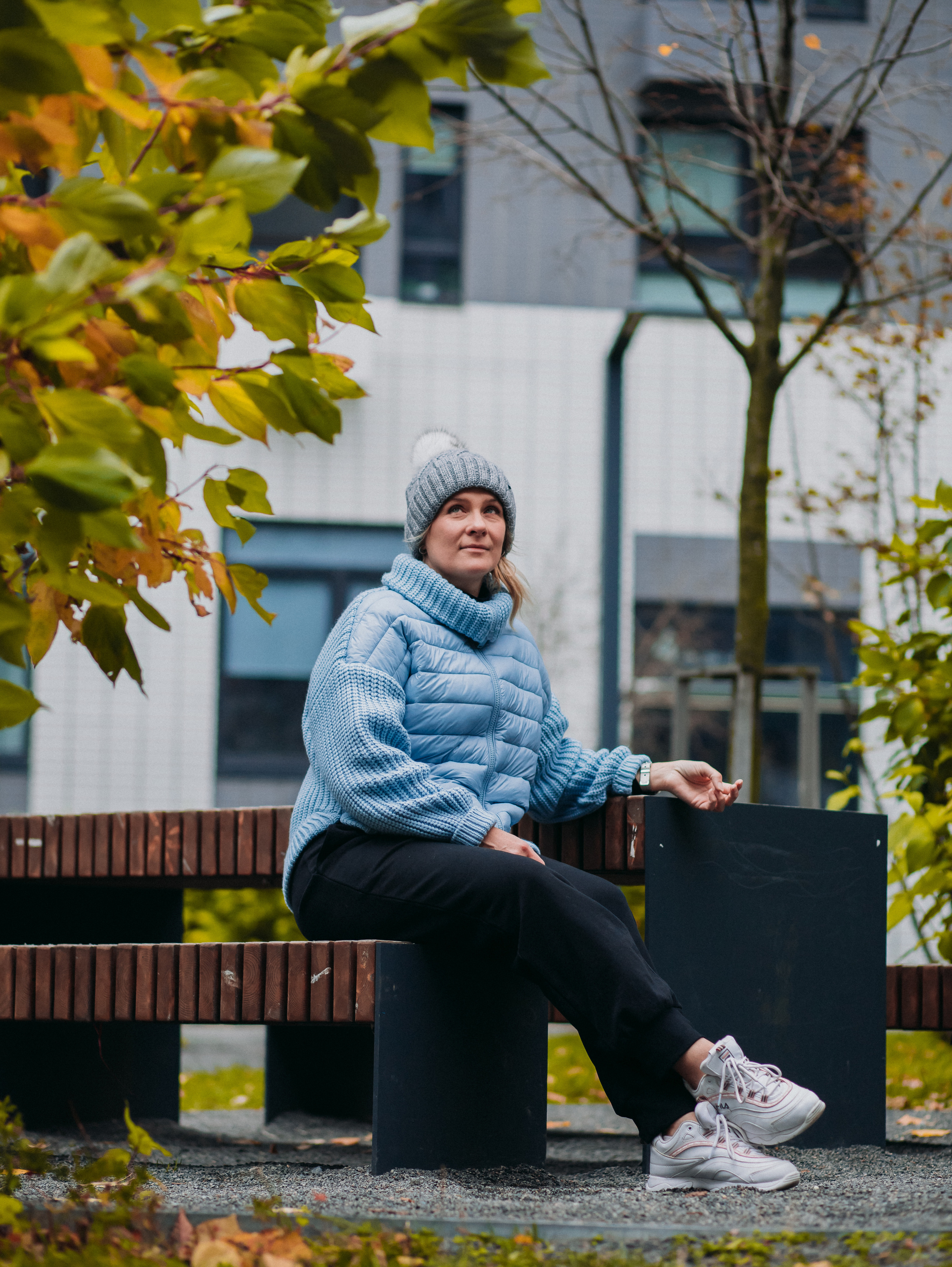 Девушка в шапке и голубой куртке на фоне дома фирмы ПИК