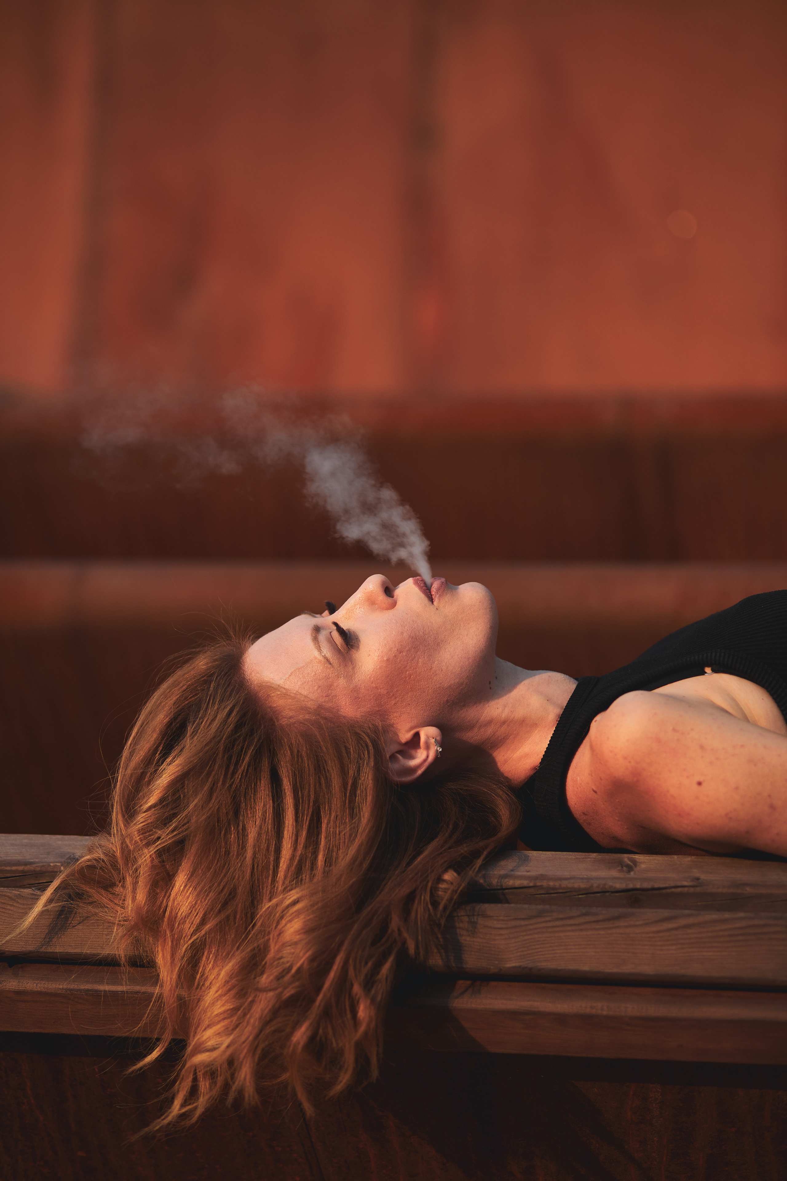 Красивая рыжеволосая девушка курит вейп на фоне из ржавого железа