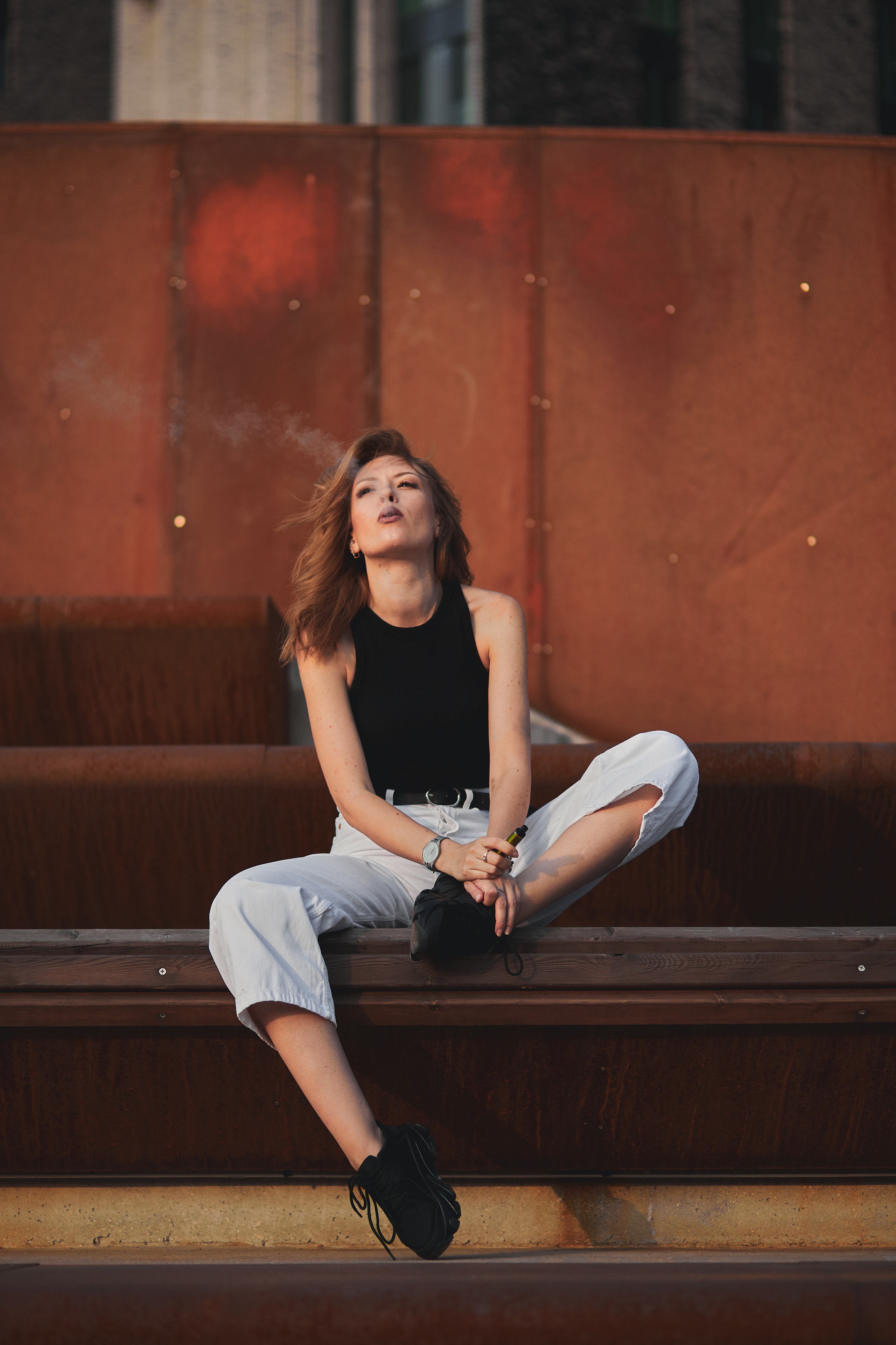 Красивая рыжеволосая девушка курит вейп на фоне из ржавого железа