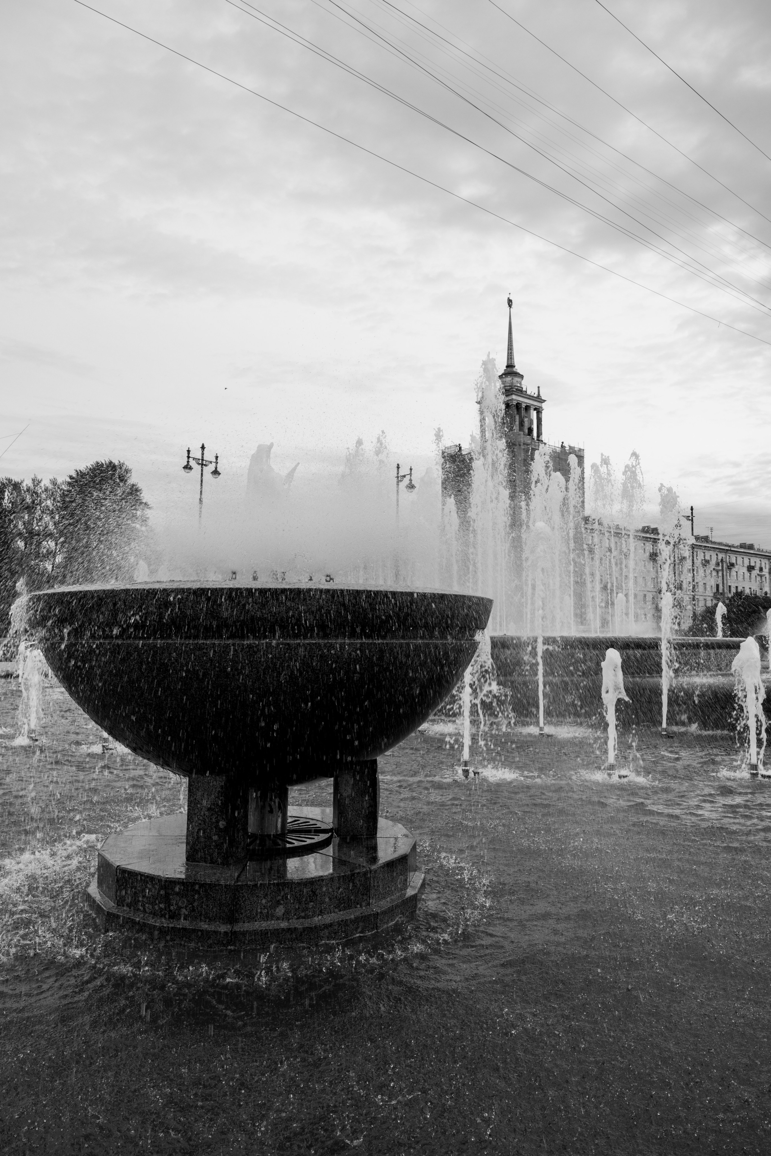 Чёрно-белая фотография фонтана со шпилем здания на заднем плане