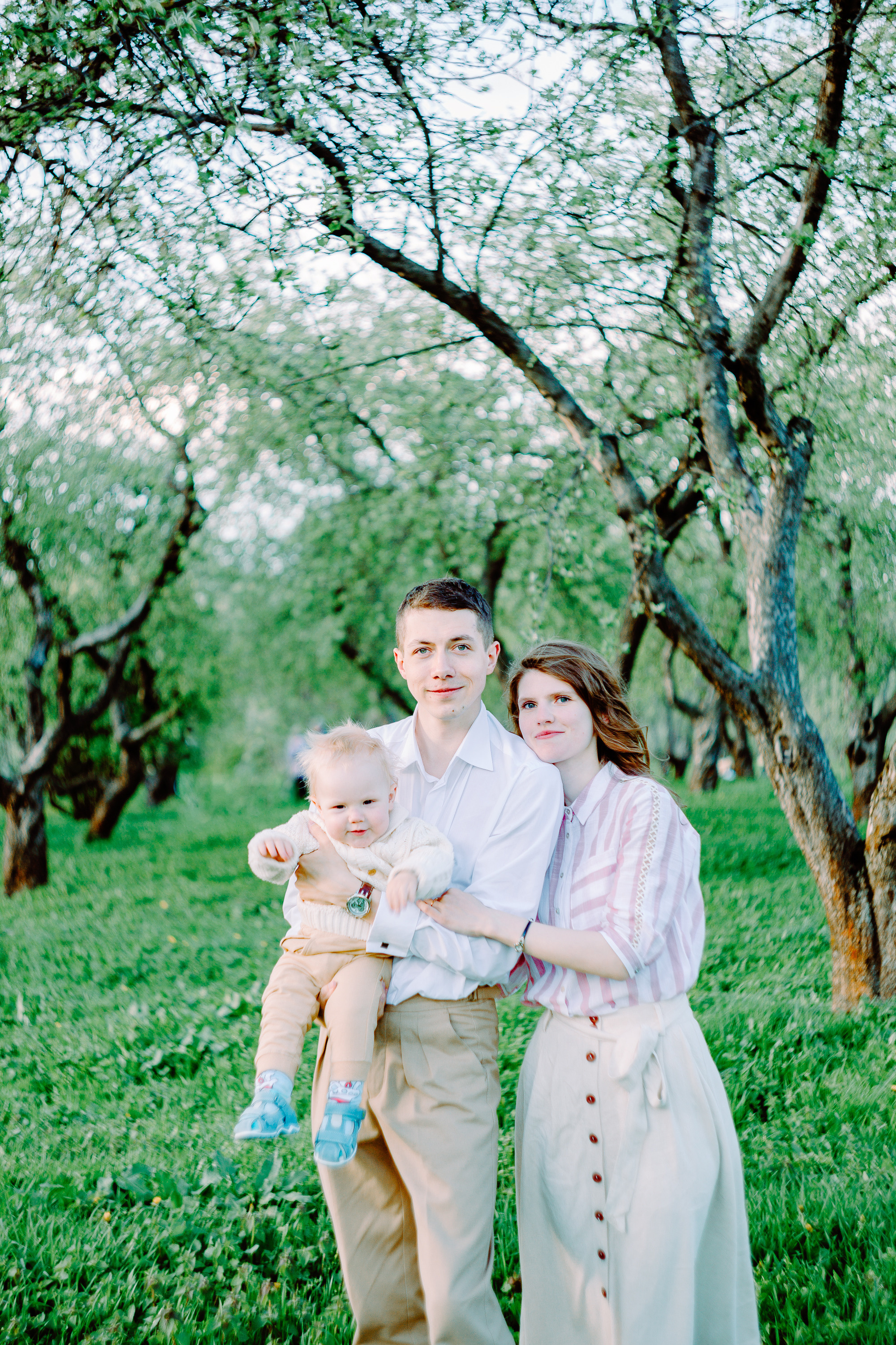 Папа, мама и малыш в саду. Вечер. Светит солнце. Кругом зелень.