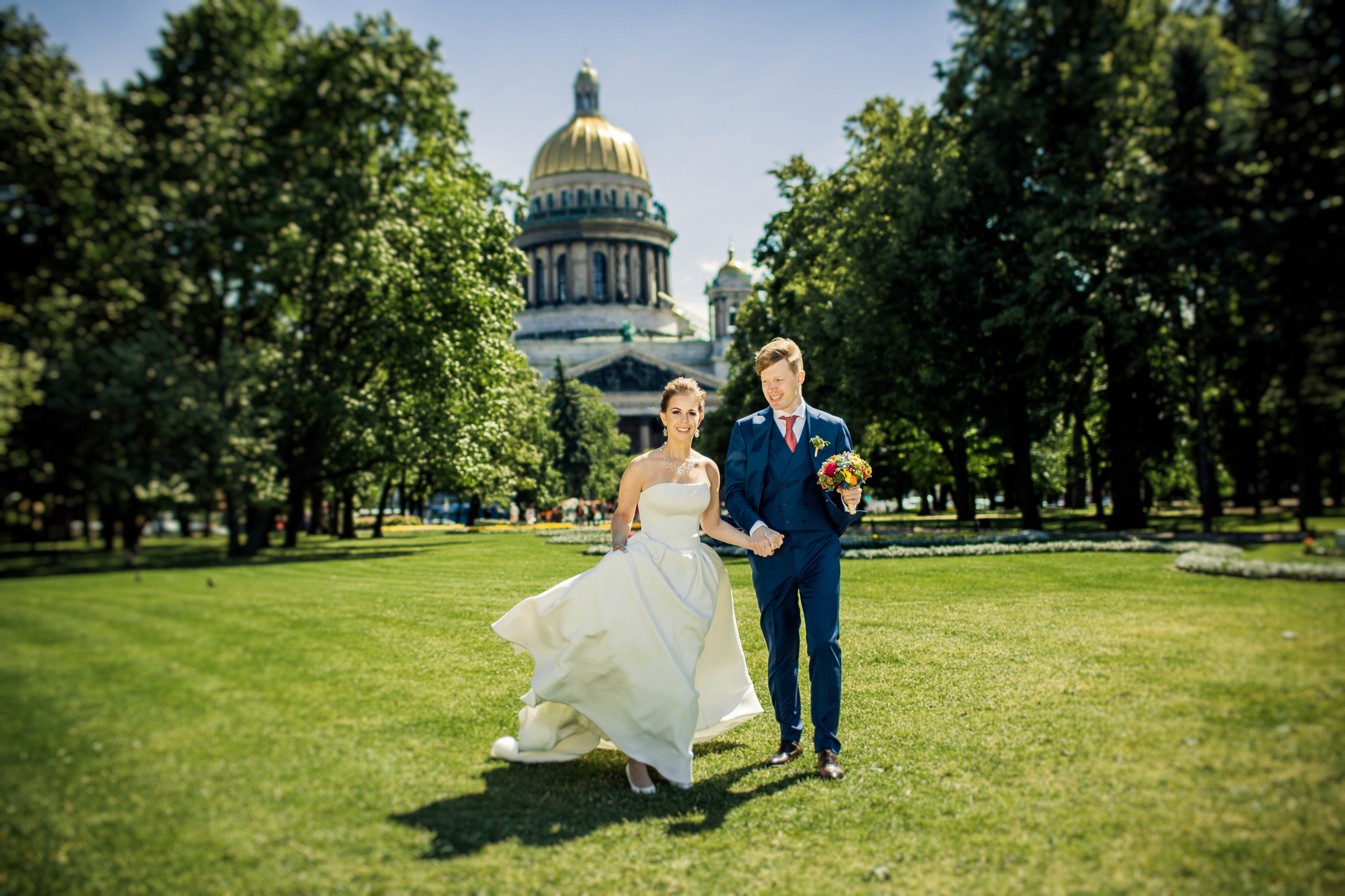 жених с невестой идут по зеленому газону около Исаакиевского собора