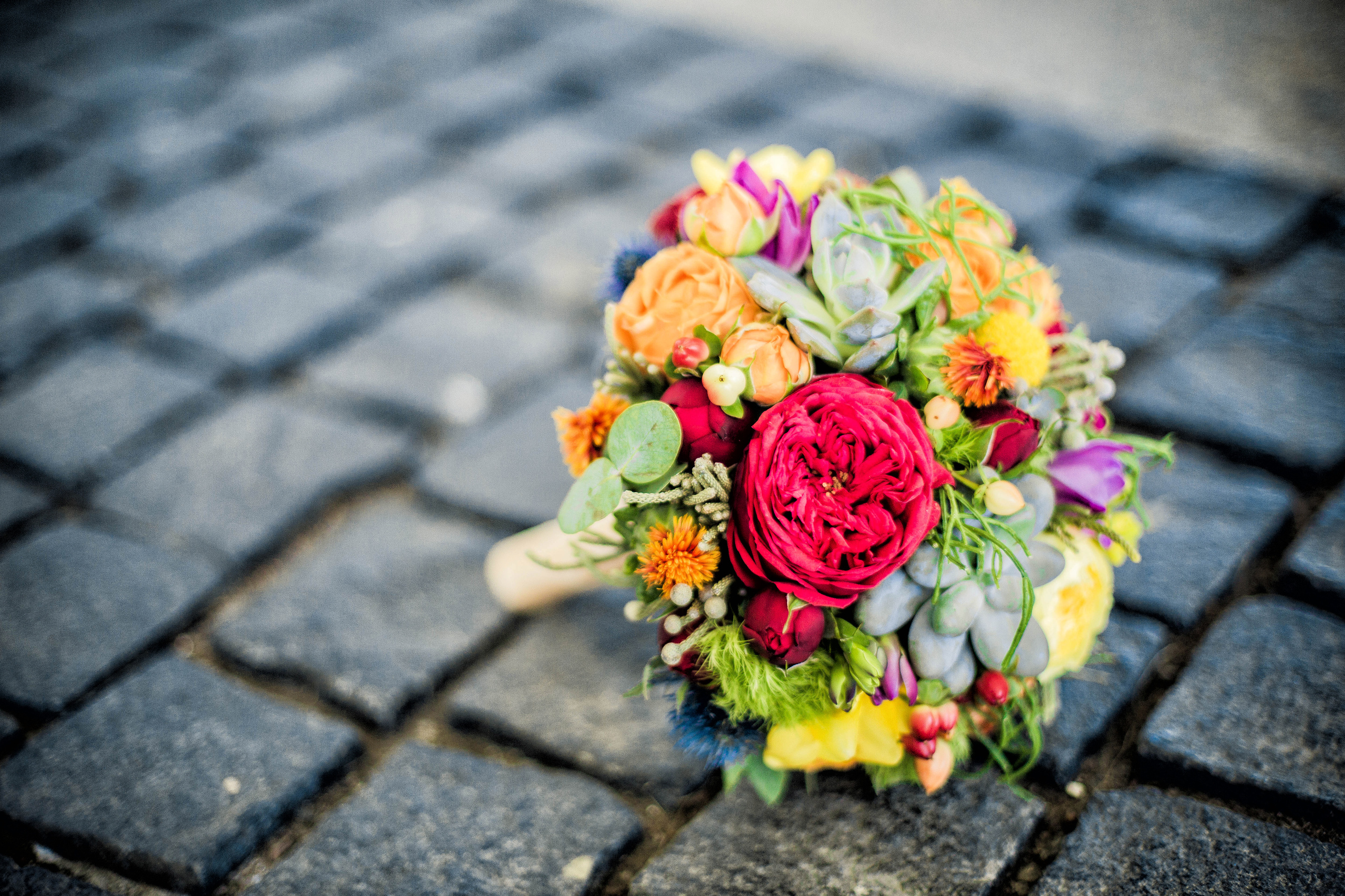 букет невесты из разноцветных цветов красиво лежит на каменной мостовой
