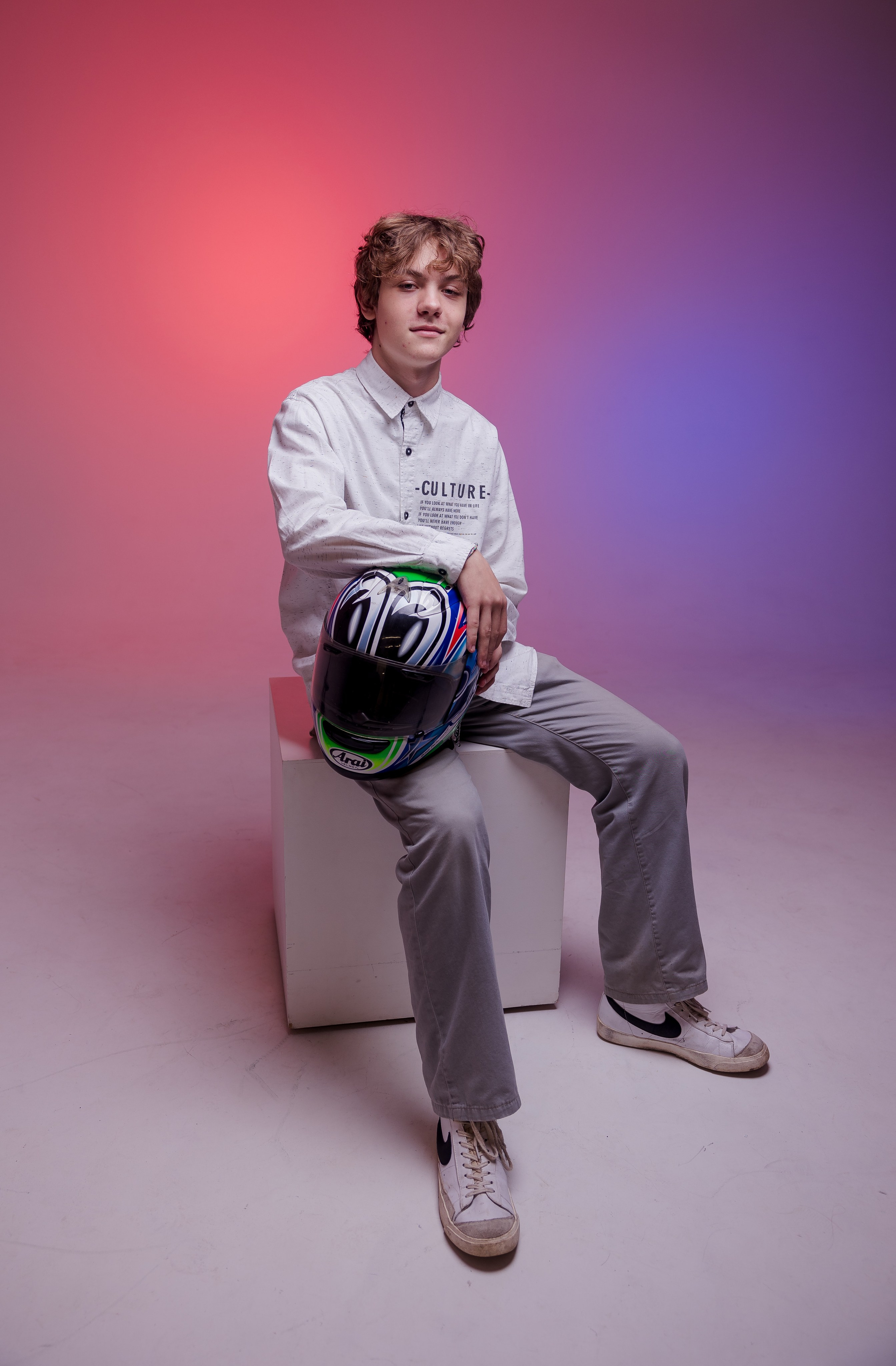 Молодой человек сидит на тумбе в фотостудии с цветным светом и держит в руках глобус