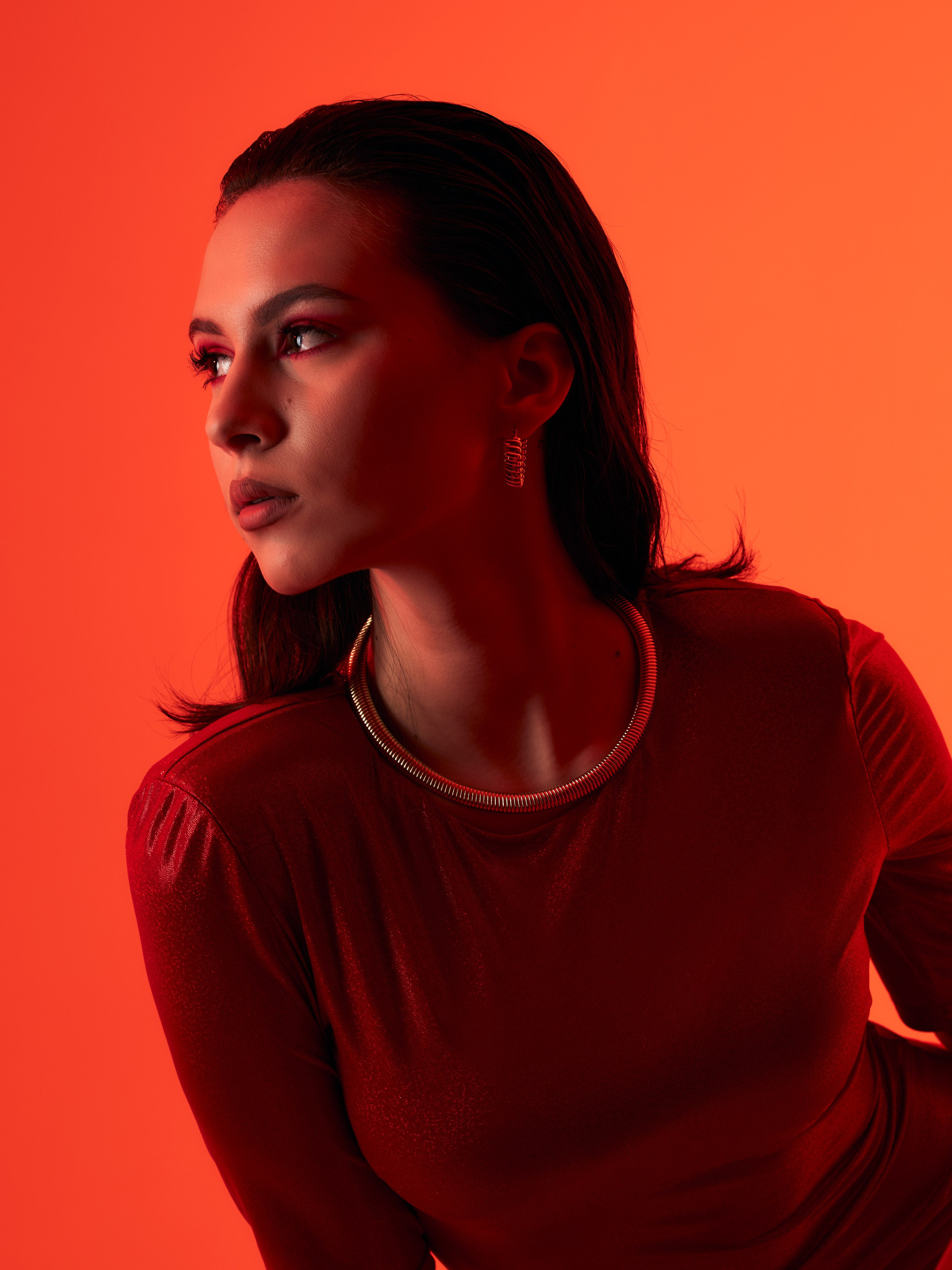 Портрет девушки-брюнетки с длинными волосами и причёской "мокрый-эффект" на красно-оранжевом фоне