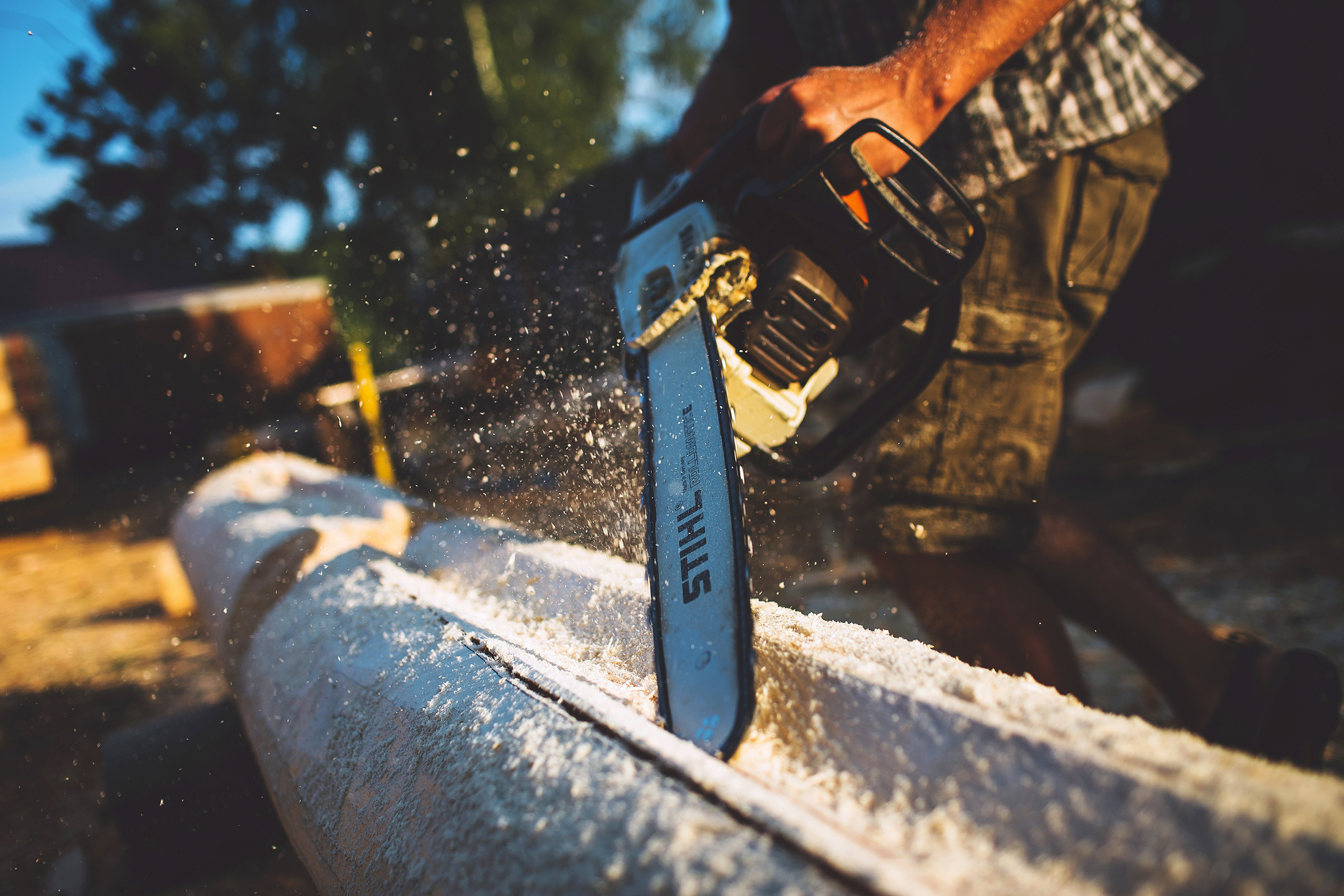 Строитель обрабатывает брус бензопилой