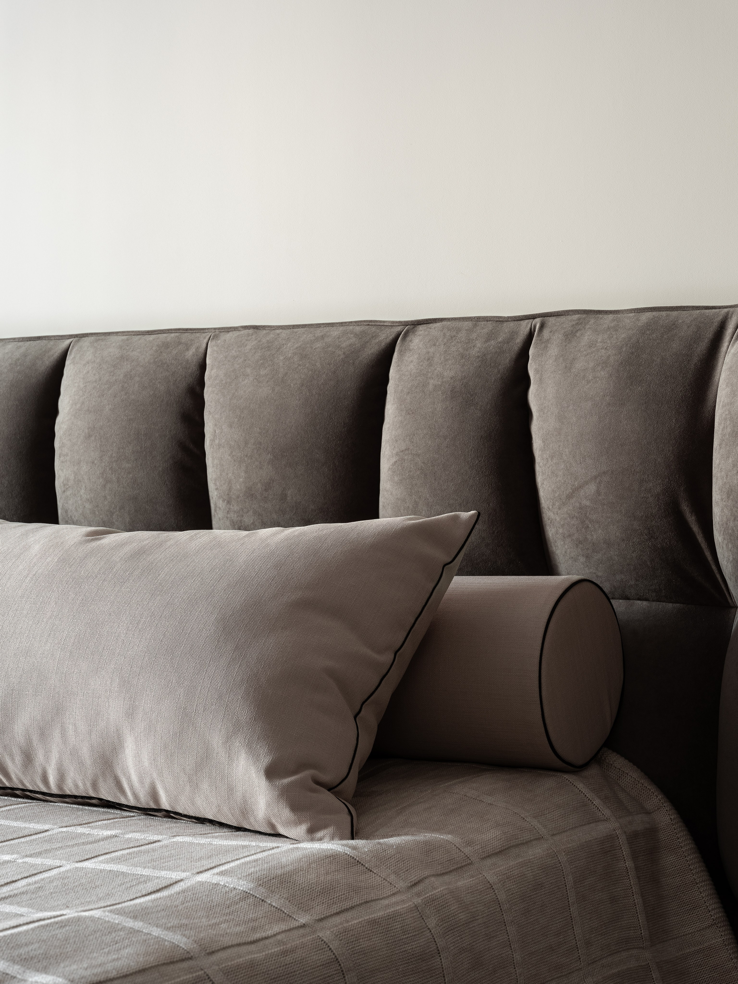 Интерьер спальни с мягким серым изголовьем, декоративной подушкой и цилиндрическим валиком, дизайнер Екатерина Мищенко, фотограф Сергей Денисенко, крупный план кровати в нейтральной палитре для уюта и современного стиля.