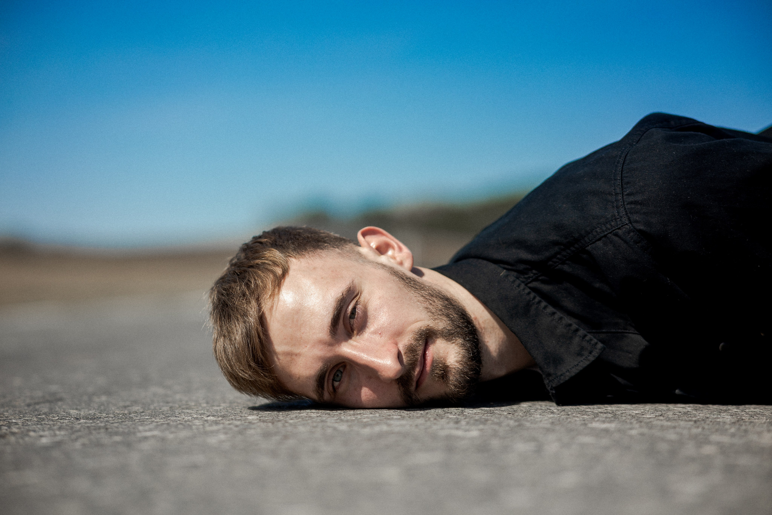 Мужчина лежит на асфальте, прямой взгляд в объектив, яркое небо, Тавда, Илья Антропов