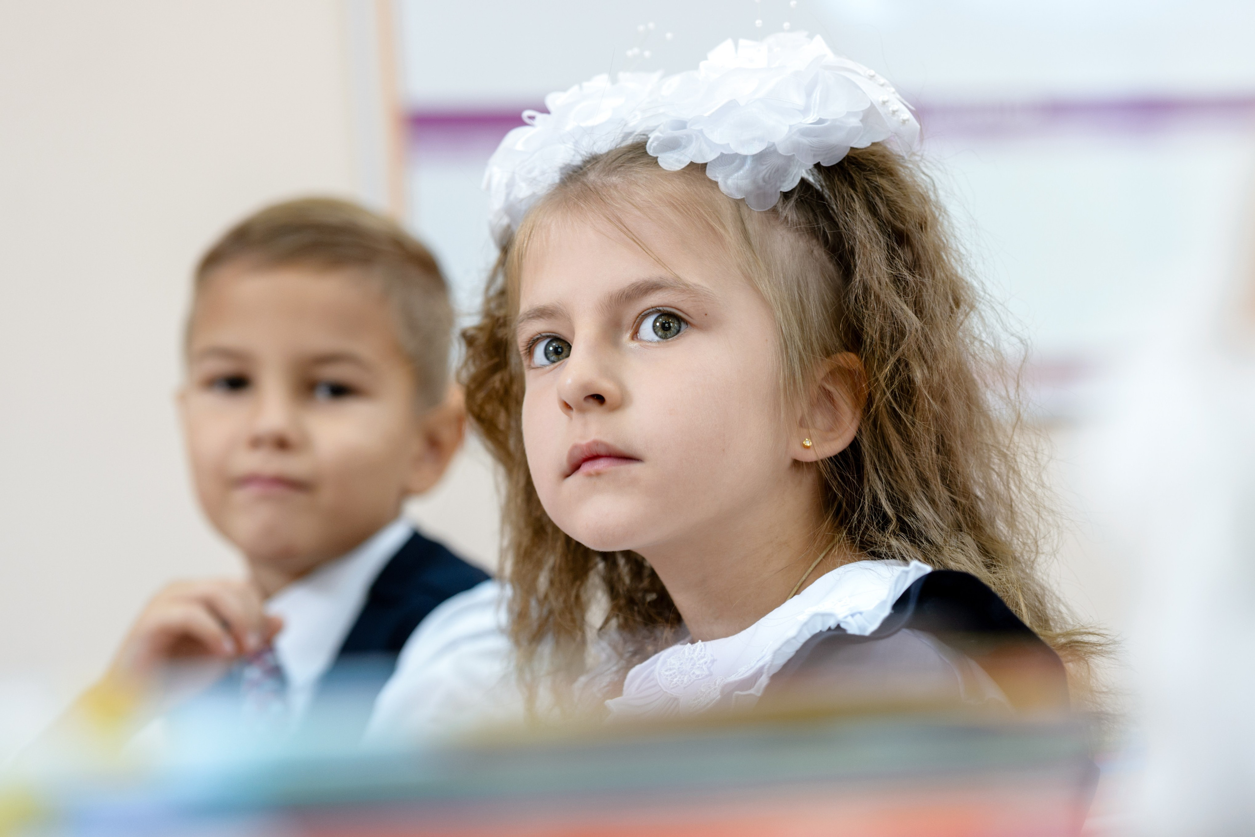 Ученица с белым бантом внимательно слушает на уроке