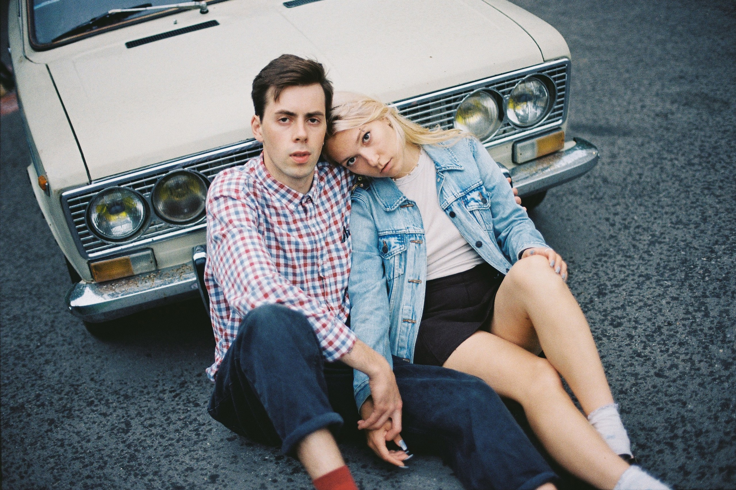 Парень с девушкой сидят в обнимку у капота автомобиля на асфальте