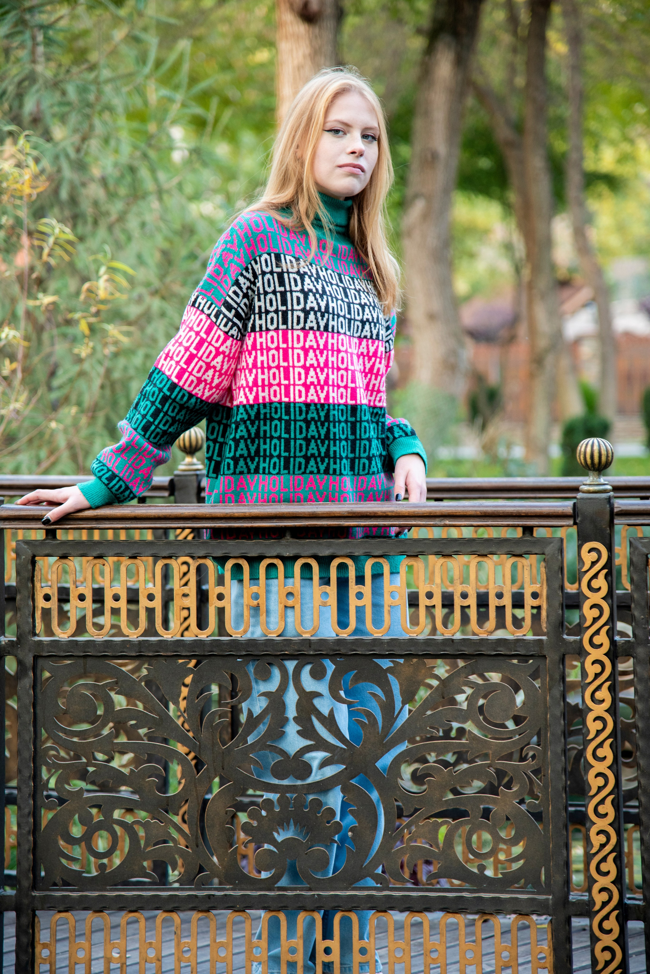 молодая девушка студентка. блондинка. длинные волосы. розово-зелёный свитер. парк Лога . осень на мостике