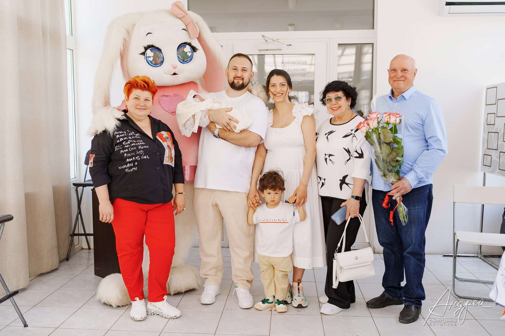 Молодые родители с новорожденной на фотозоне роддома ЦГБ в окружении гостей и ростовой куклы, Ростов-на-Дону, фотосъемка выписки