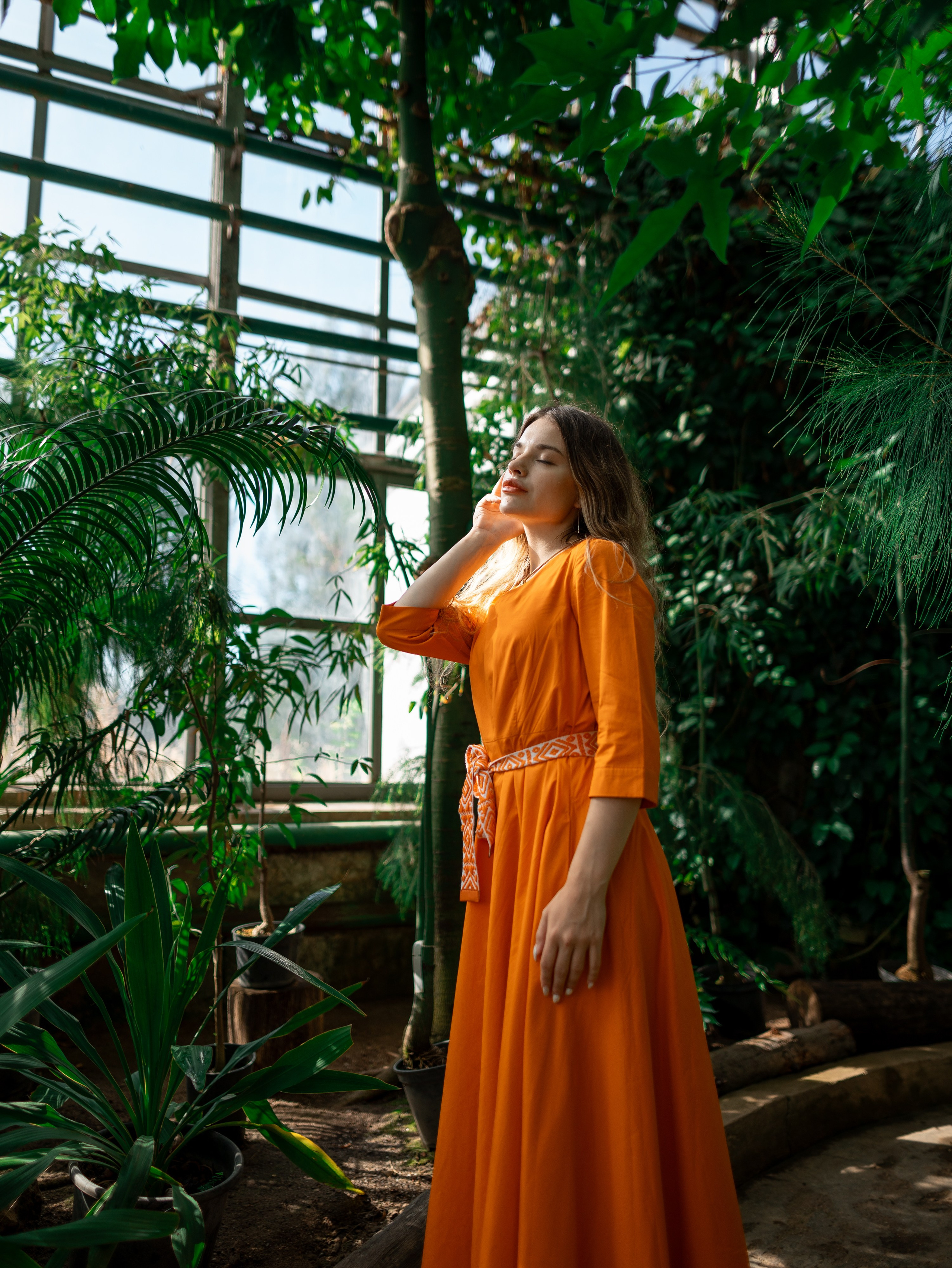 Девушка в оранжевом платье стоит на фоне зелени