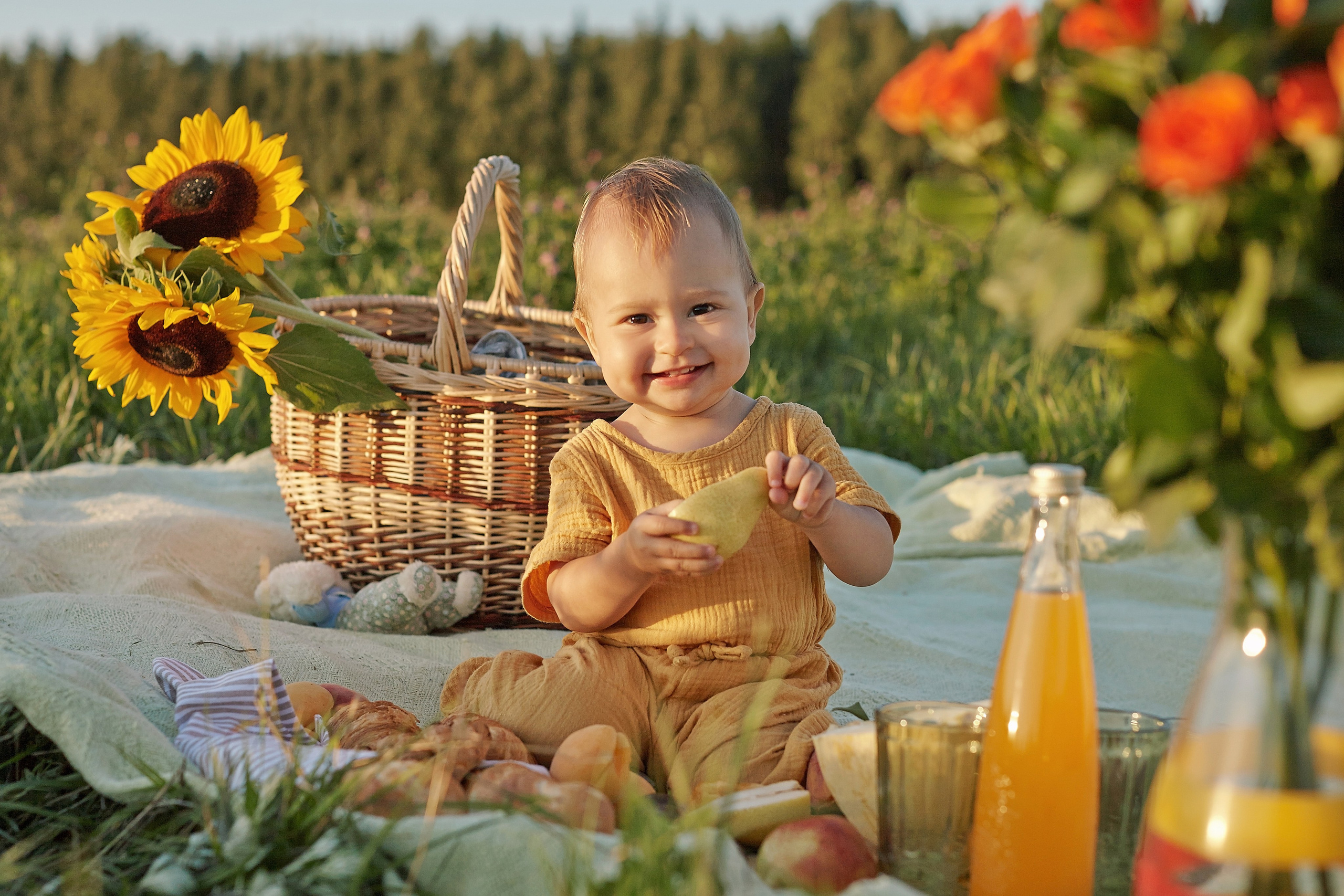 маленький ребенок улыбается на фоне подсолнухов и корзинки с выпечкой