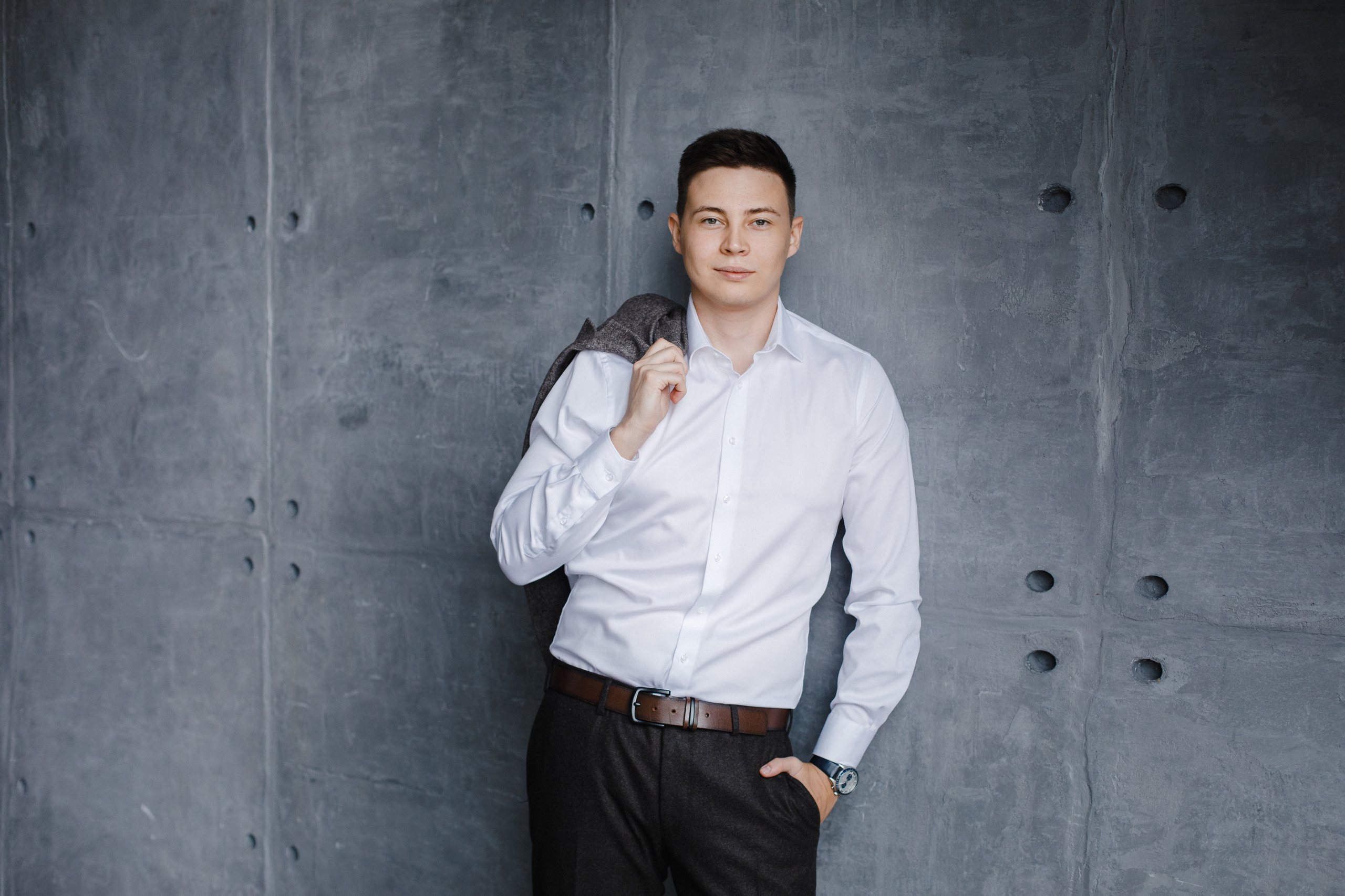 Портрет мужчины в белой рубашке на сером фактурном бетонном фоне.