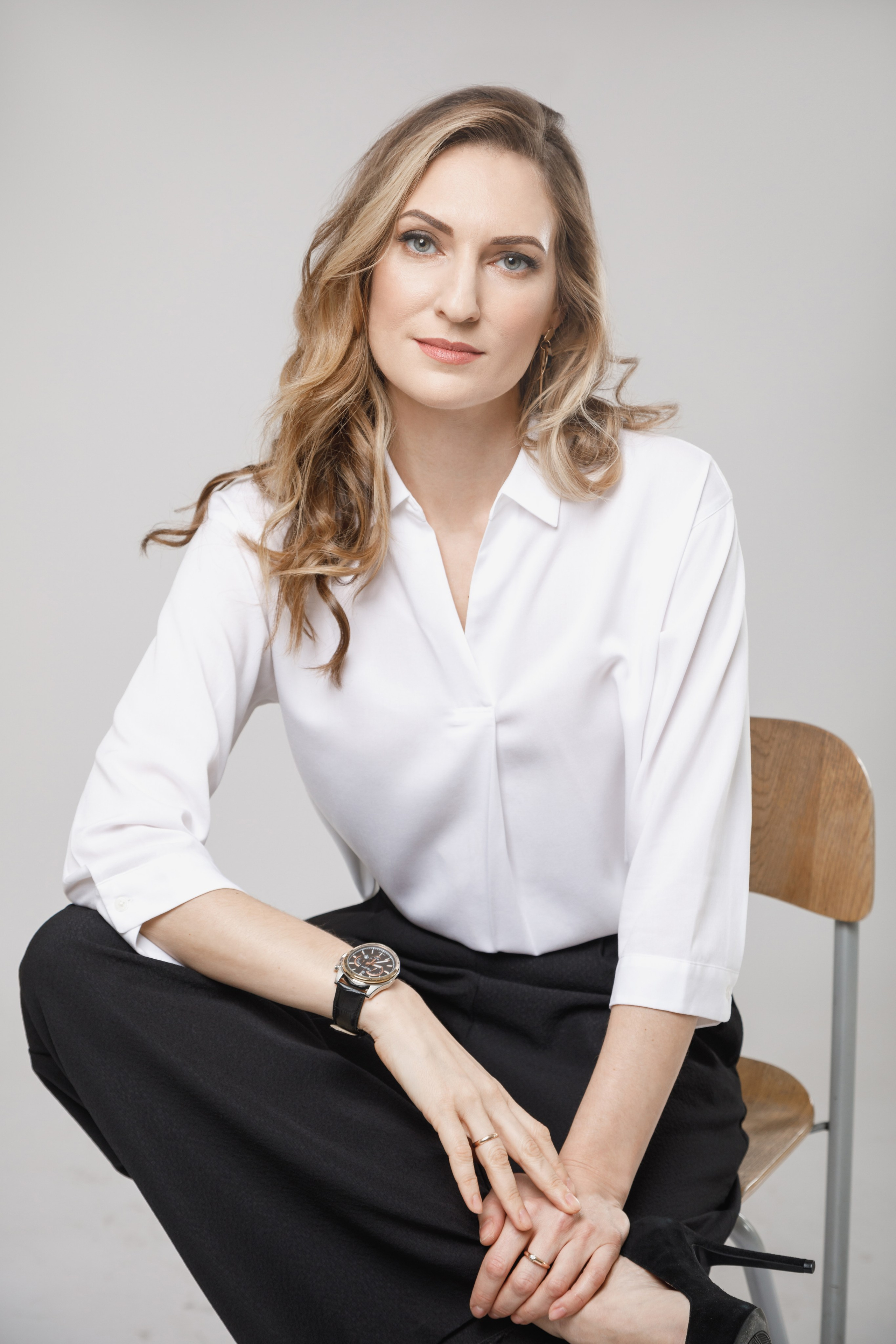 Девушка в белой рубашке сидит на стуле на светлом студийном фоне.