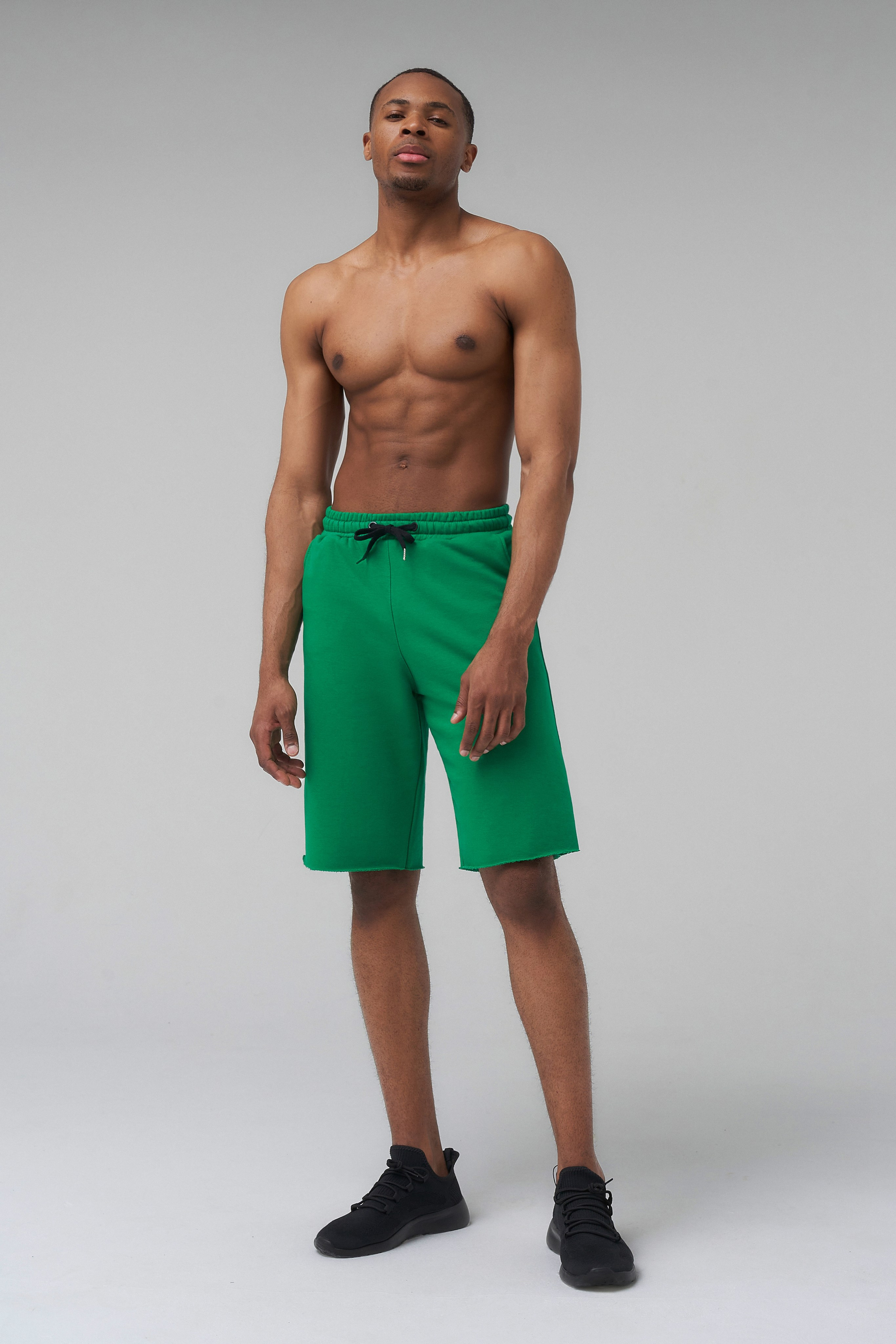 Спортивный темнокожий парень модель позирует в зеленых шортах на циклораме