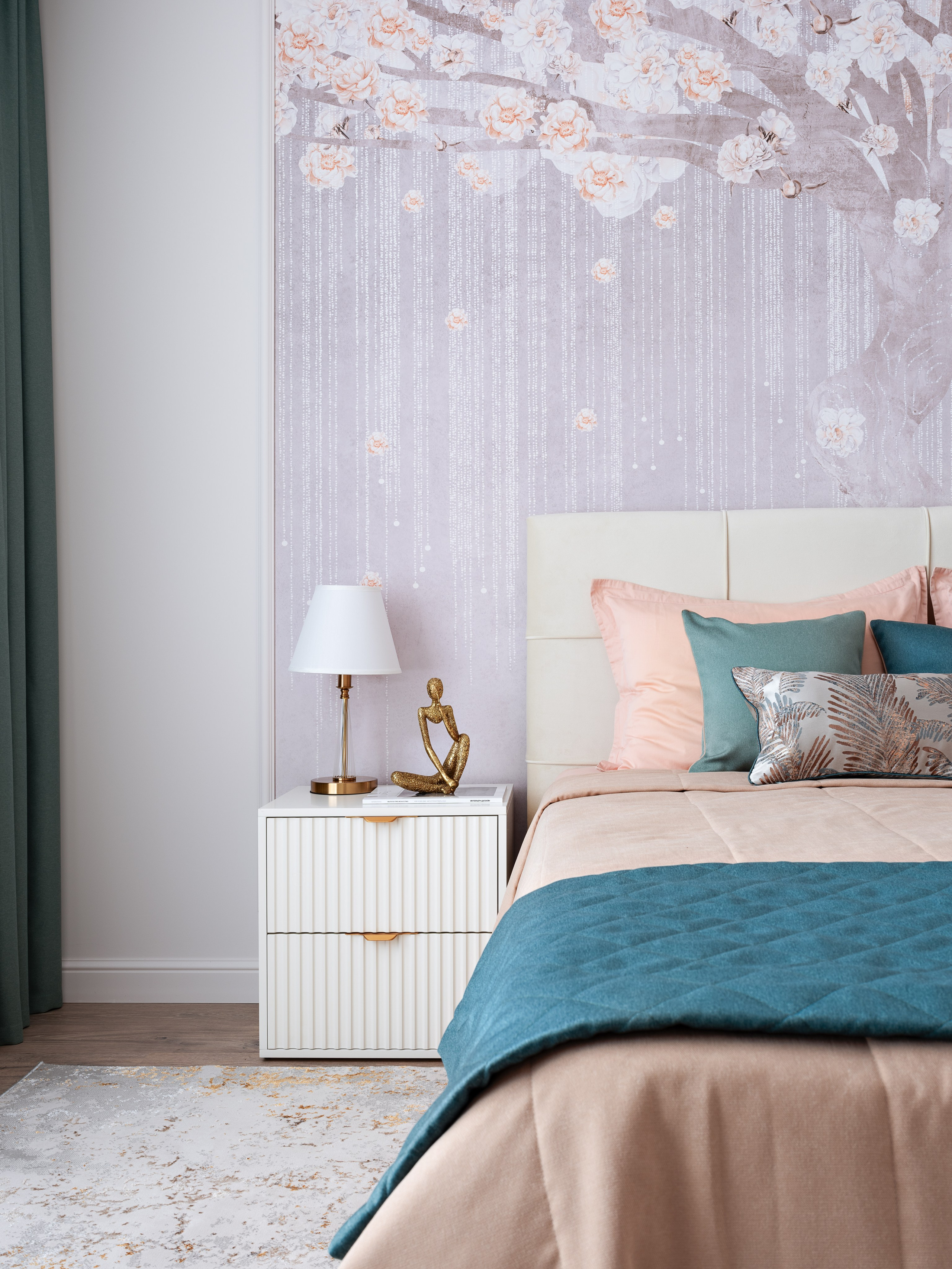 Интерьер спальни с декоративными подушками с растительным орнаментом, прикроватной тумбой с настольной лампой и изящной фигуркой, акцентной стеной с флористическими обоями. Проект дизайнера Натальи Бунеевой, стилизация от Натальи Якушевой, фотограф Сергей Денисенко.