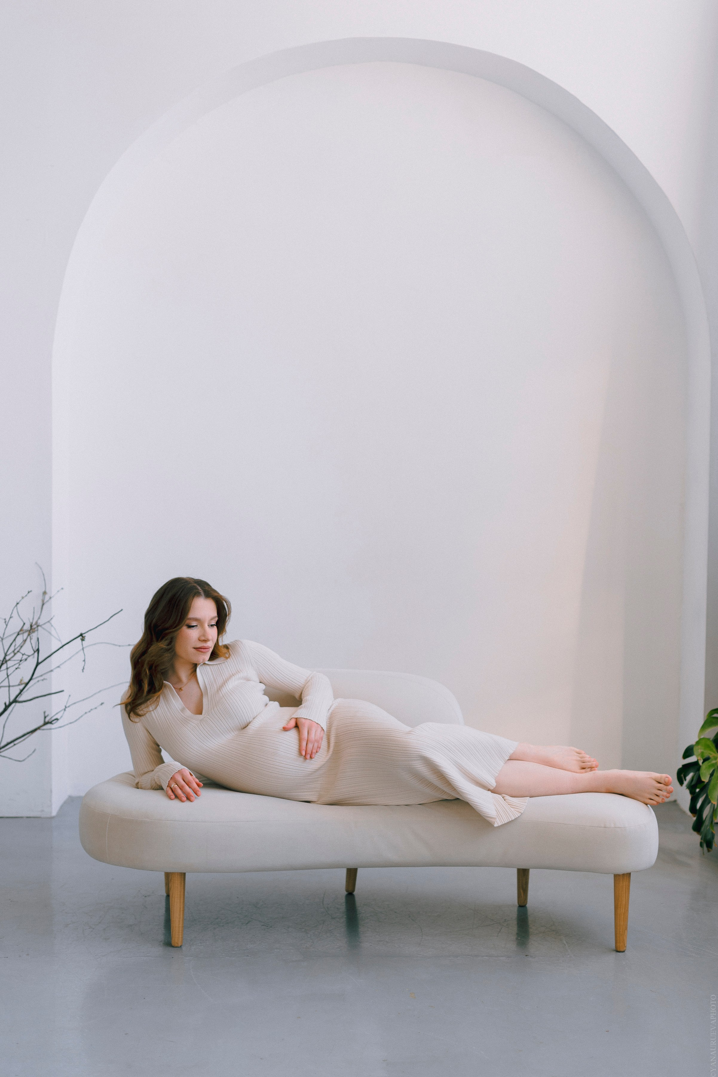 Беременная девушка лежит на диване в бежевом платье