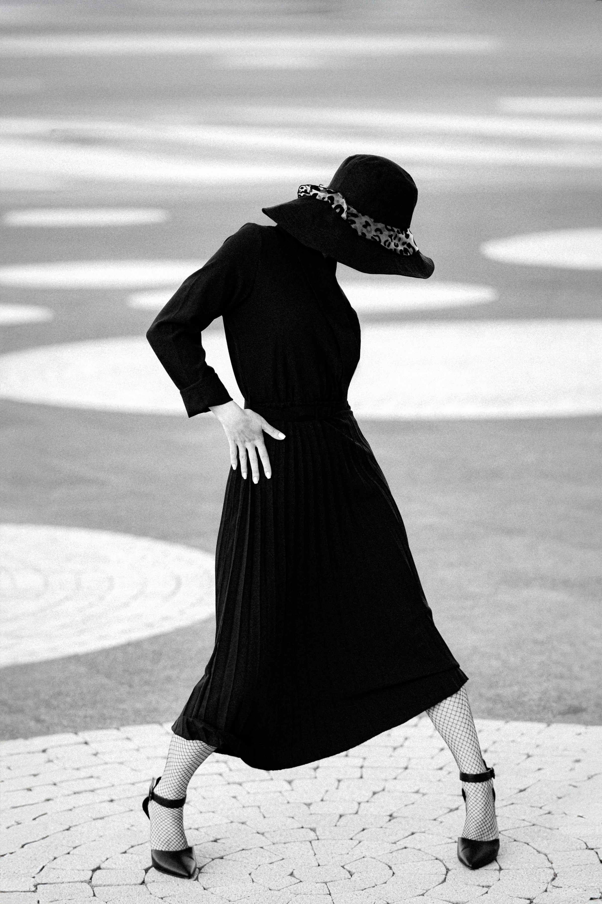 Женщина в чёрной шляпе и платье позирует на фоне геометрических кругов, чёрно-белая арт-фотография в стиле минимализма