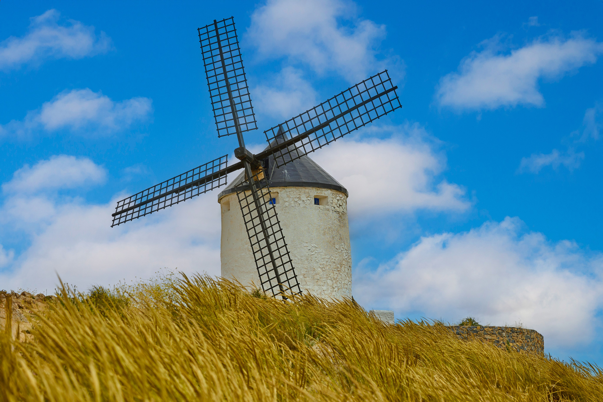 Historic windmill in Consuegra, Castilla-La Mancha, with golden wheat and clear blue sky