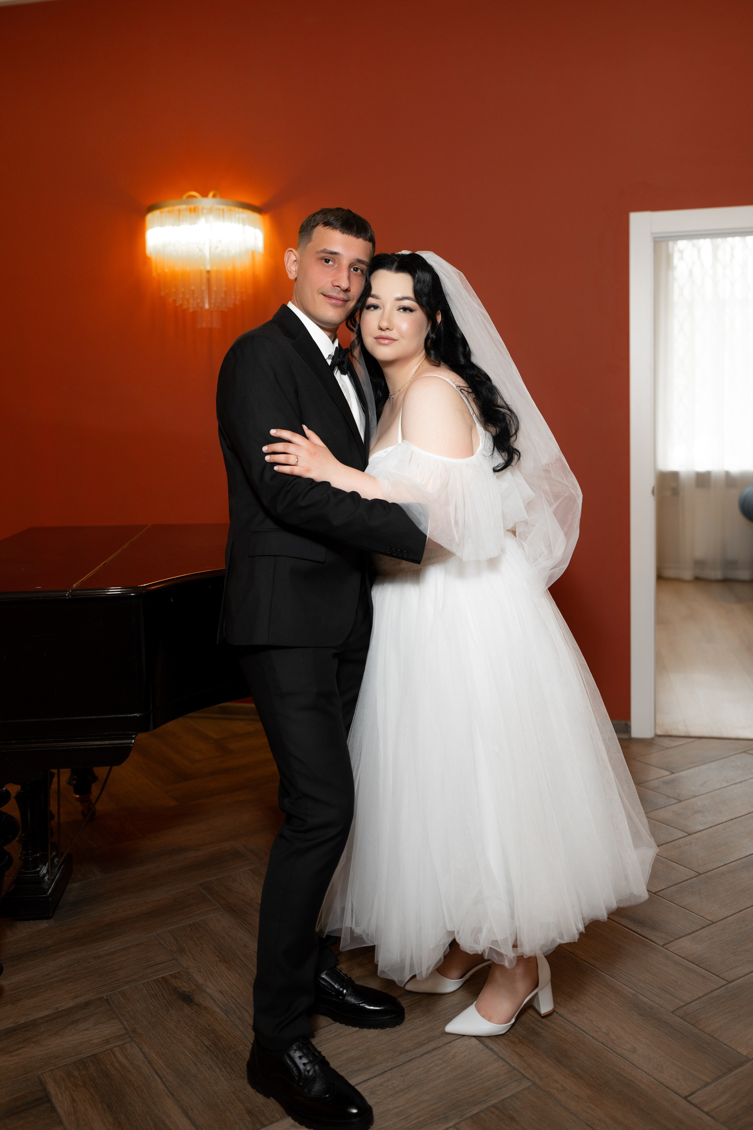 Свадебная фотосессия  в загсе Фрунзенского района на проспекте Славы в Санкт Петербурге жених обнимает невесту в красном зале