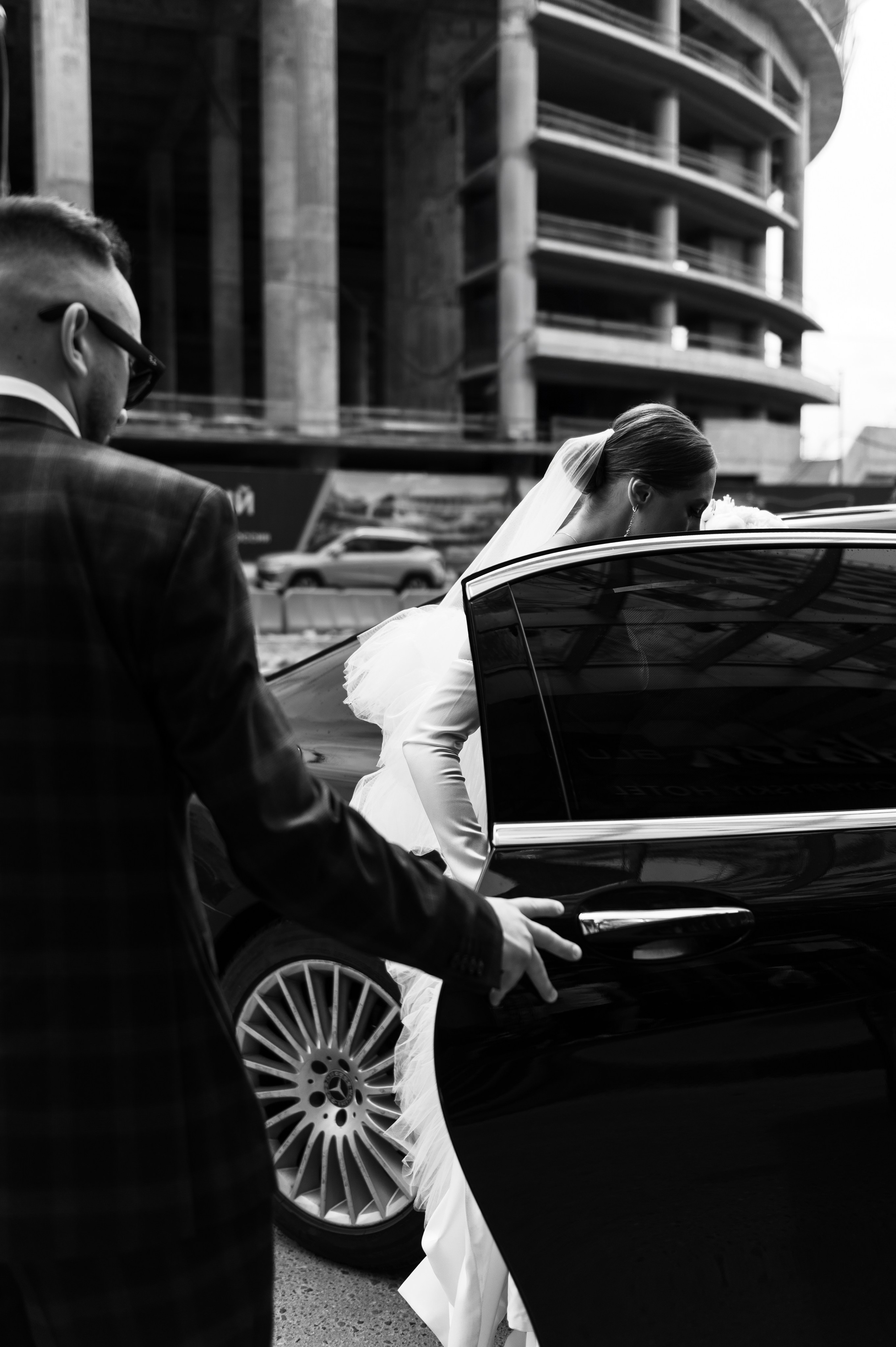 Невеста садится в машину, жених держит дверь.