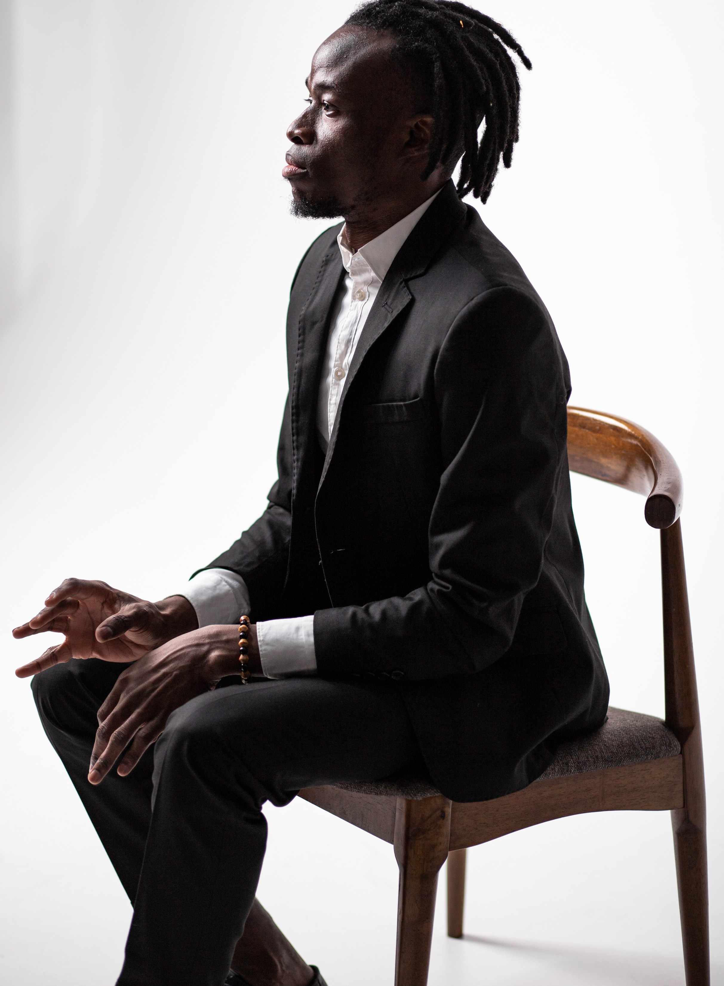 Афроамериканец играет на воображаемом пианино. Негр в костюме. Чернокожий парень сидит на стуле.