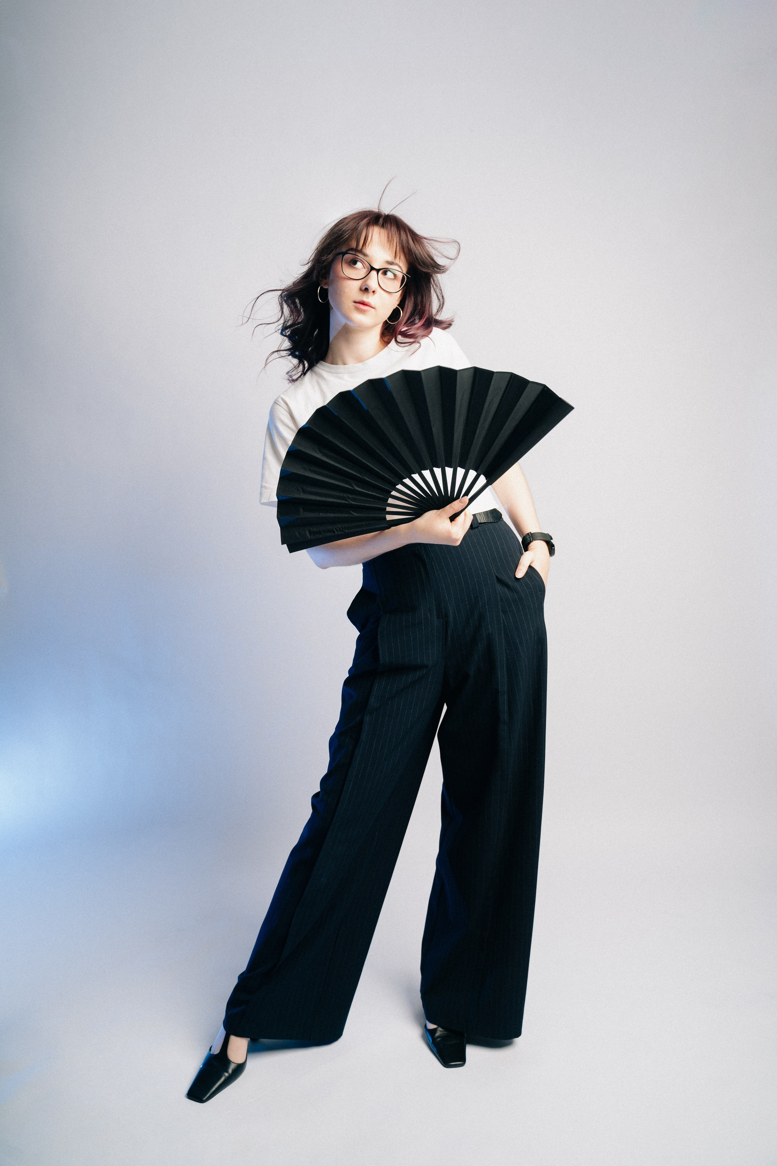 Модель танцует с черным веером в минималистичной студийной постановке.