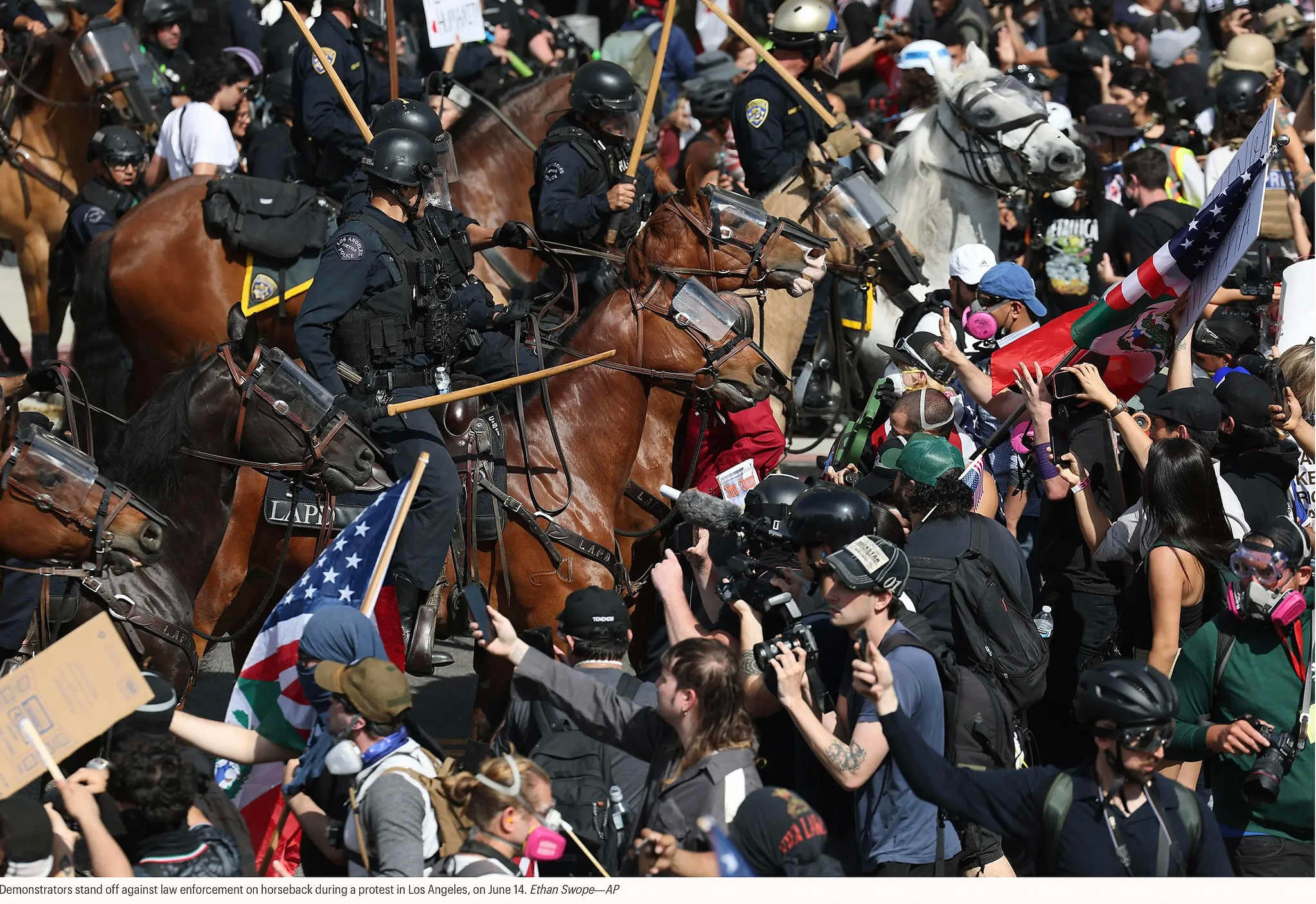 Демонстранты противостоят конным полицейским во время акции протеста в Лос-Анджелесе, 14 июня. Итан Своуп — AP