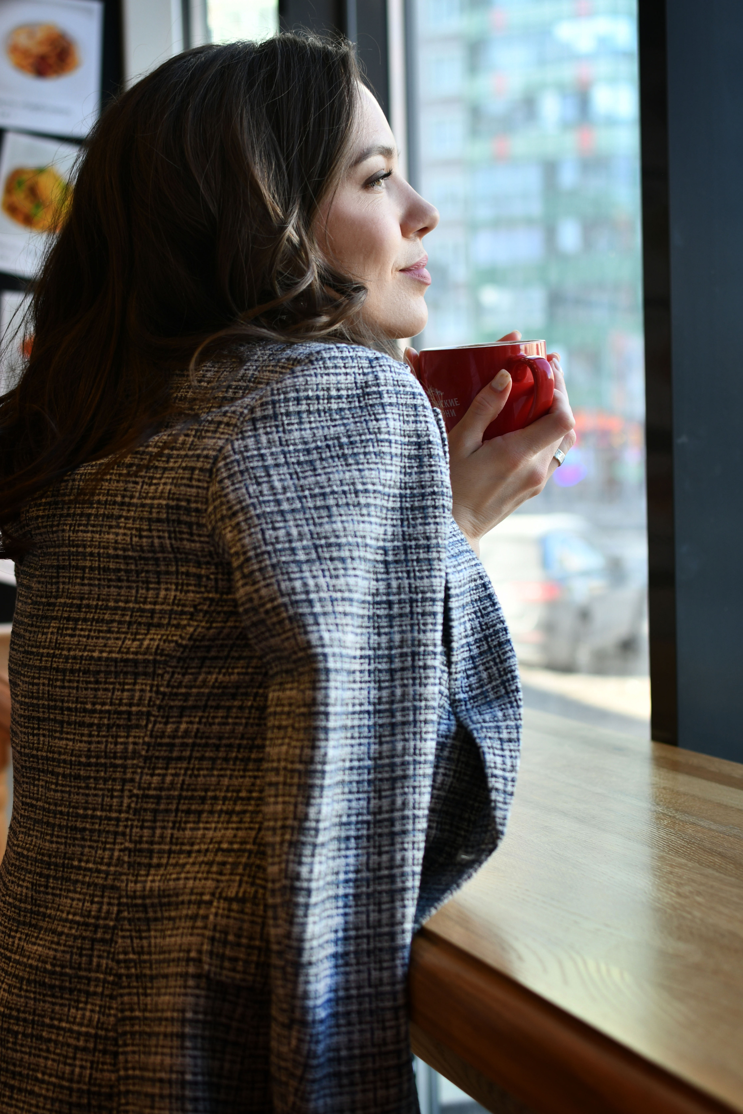 Девушка задумчиво смотрит в окно в кафе