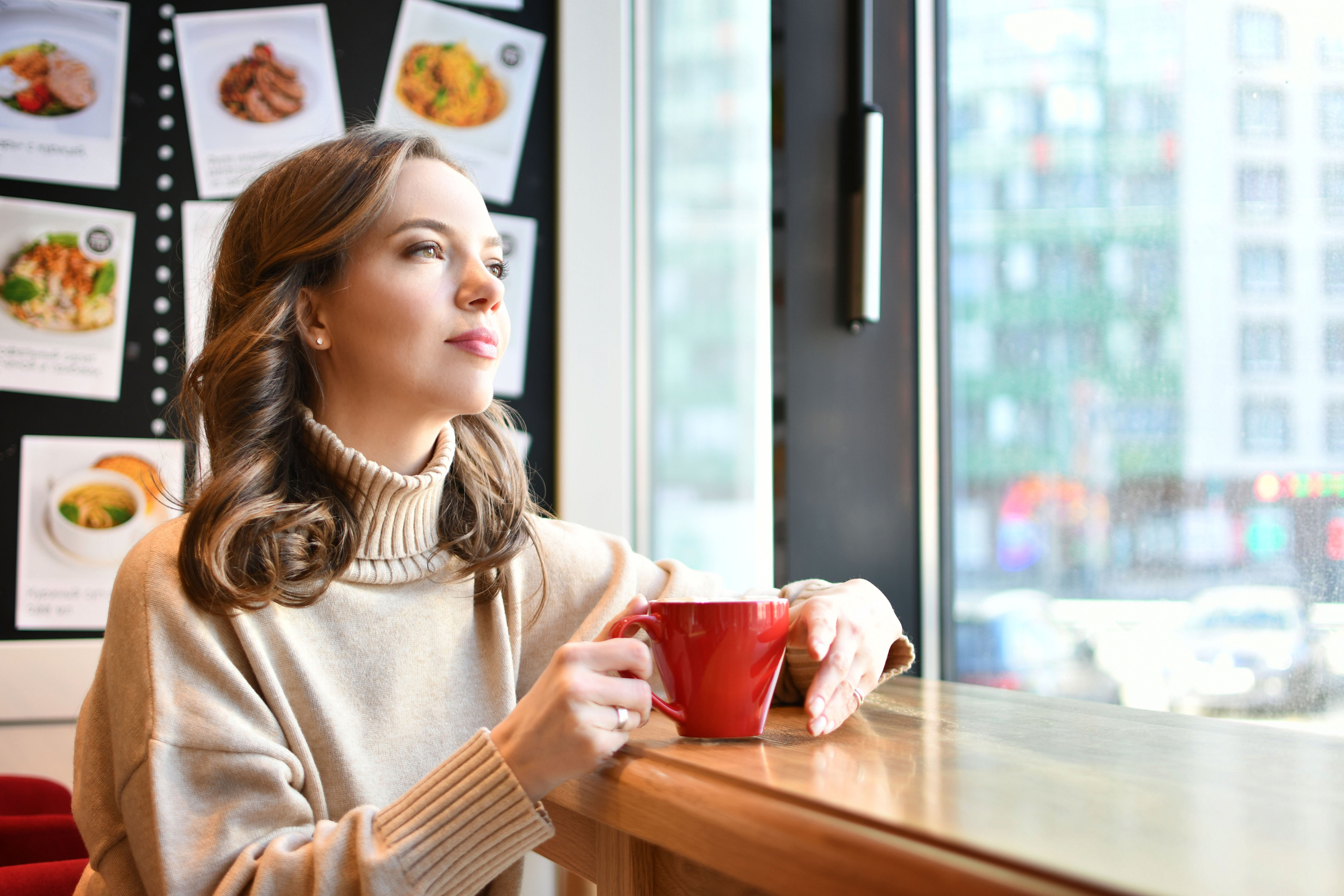 Девушка сидит в кафе у окна и смотрит в окно