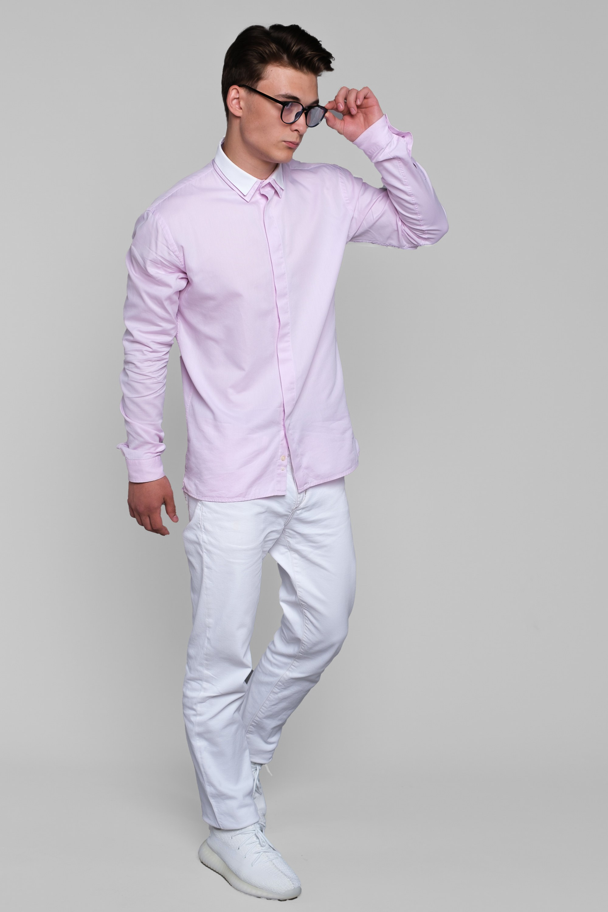 Молодой человек в очках стоит в розовой рубашке, белых брюках и белых ботинках. Вид спереди. Фото для маркетплейсов