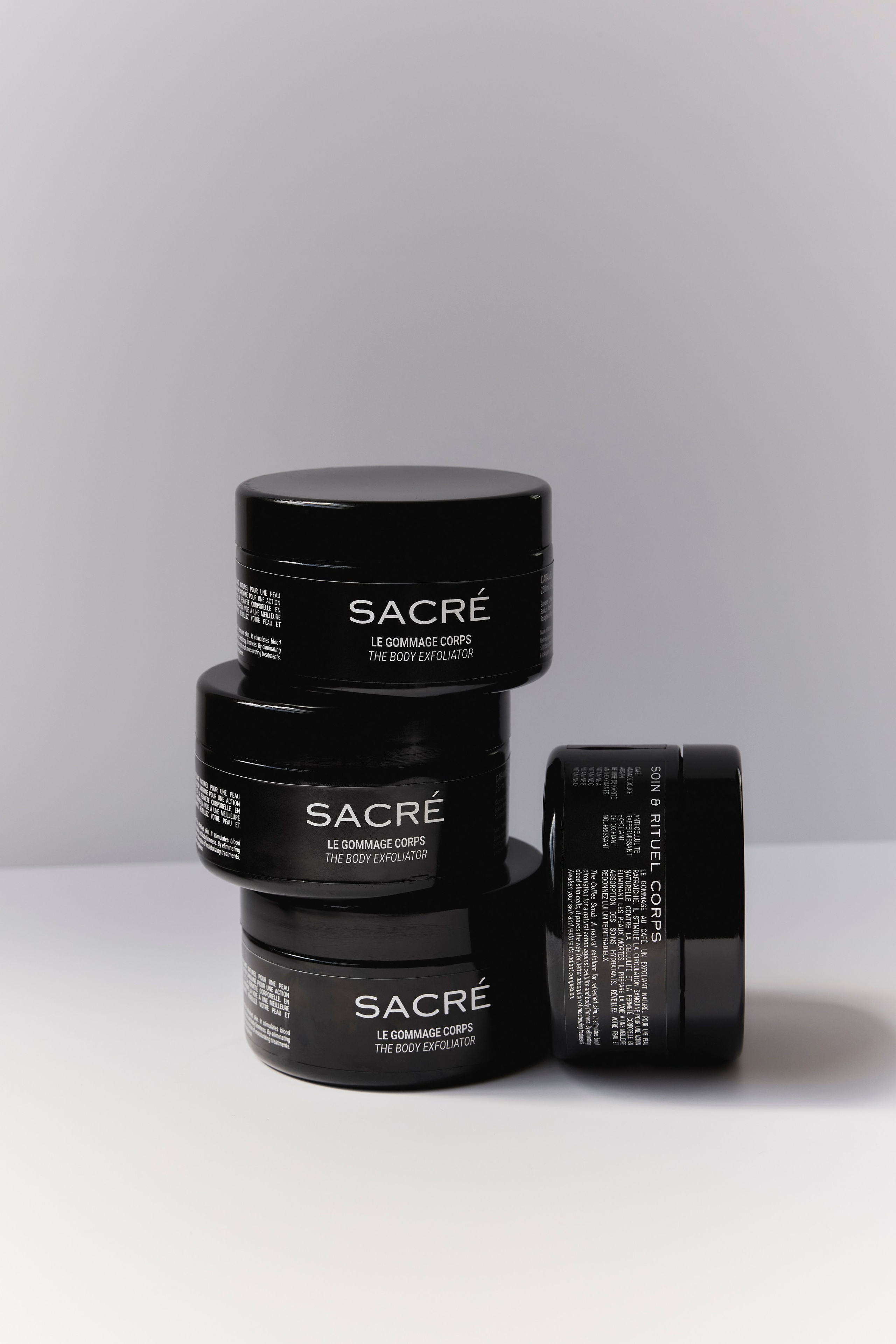 Stack of black scrub jars on a white surface, emphasizing minimalist beauty product design.