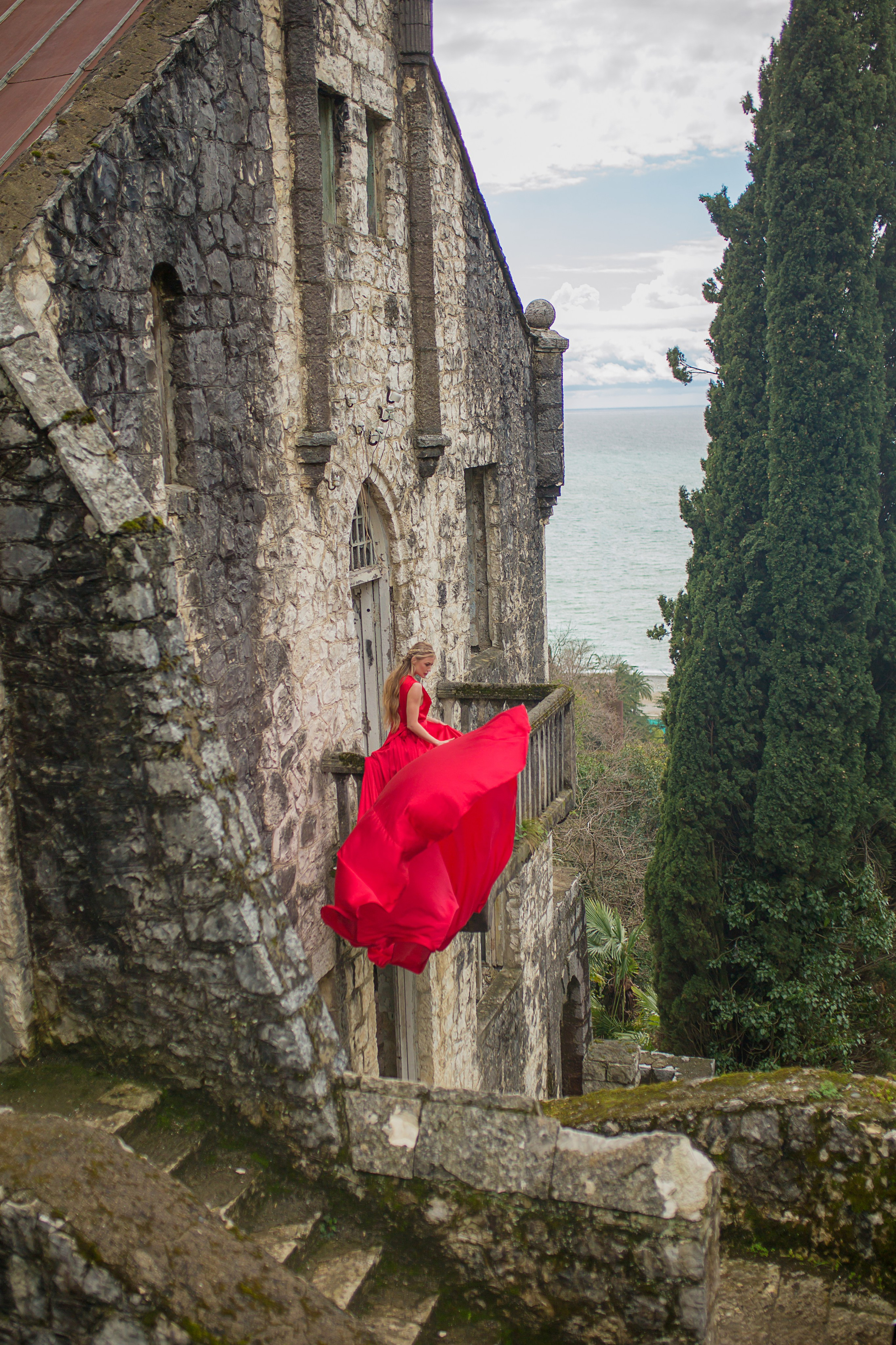 Девушка блондинка сидит в красном платье на балконе заброшенного здания